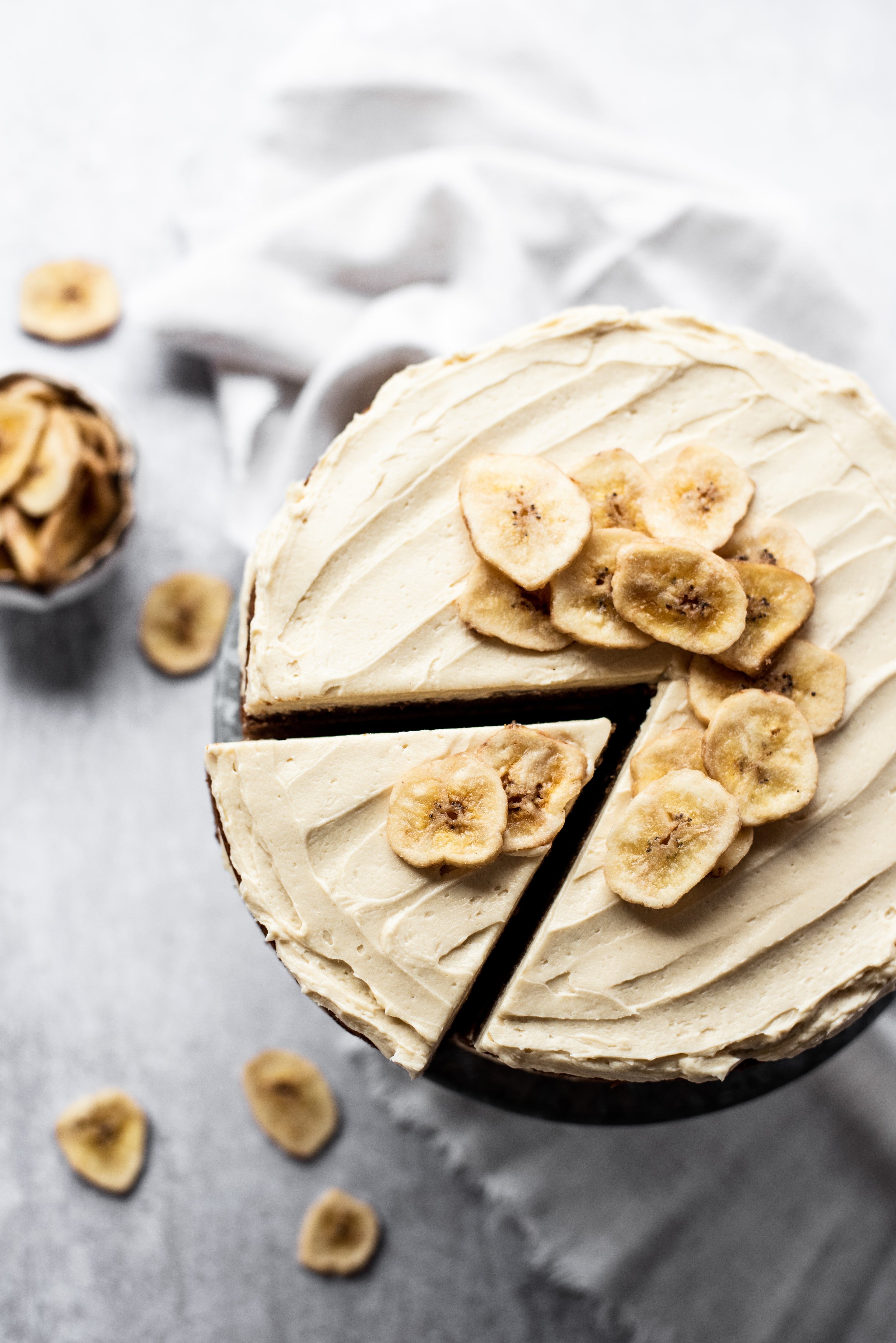 Top down image of banana layer cake with slice cut and topped with banana chips