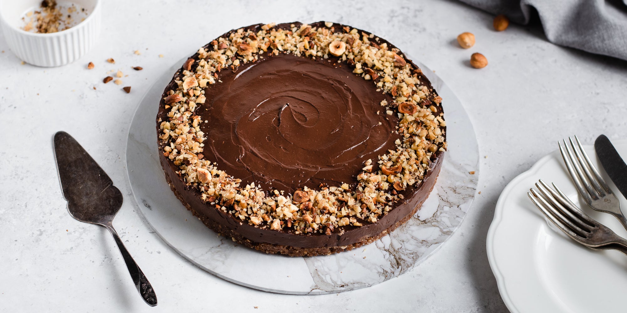 Top view of Raw Chocolate Avocado Cheesecake on a marble serving board, next to a cake knife and plates with forks