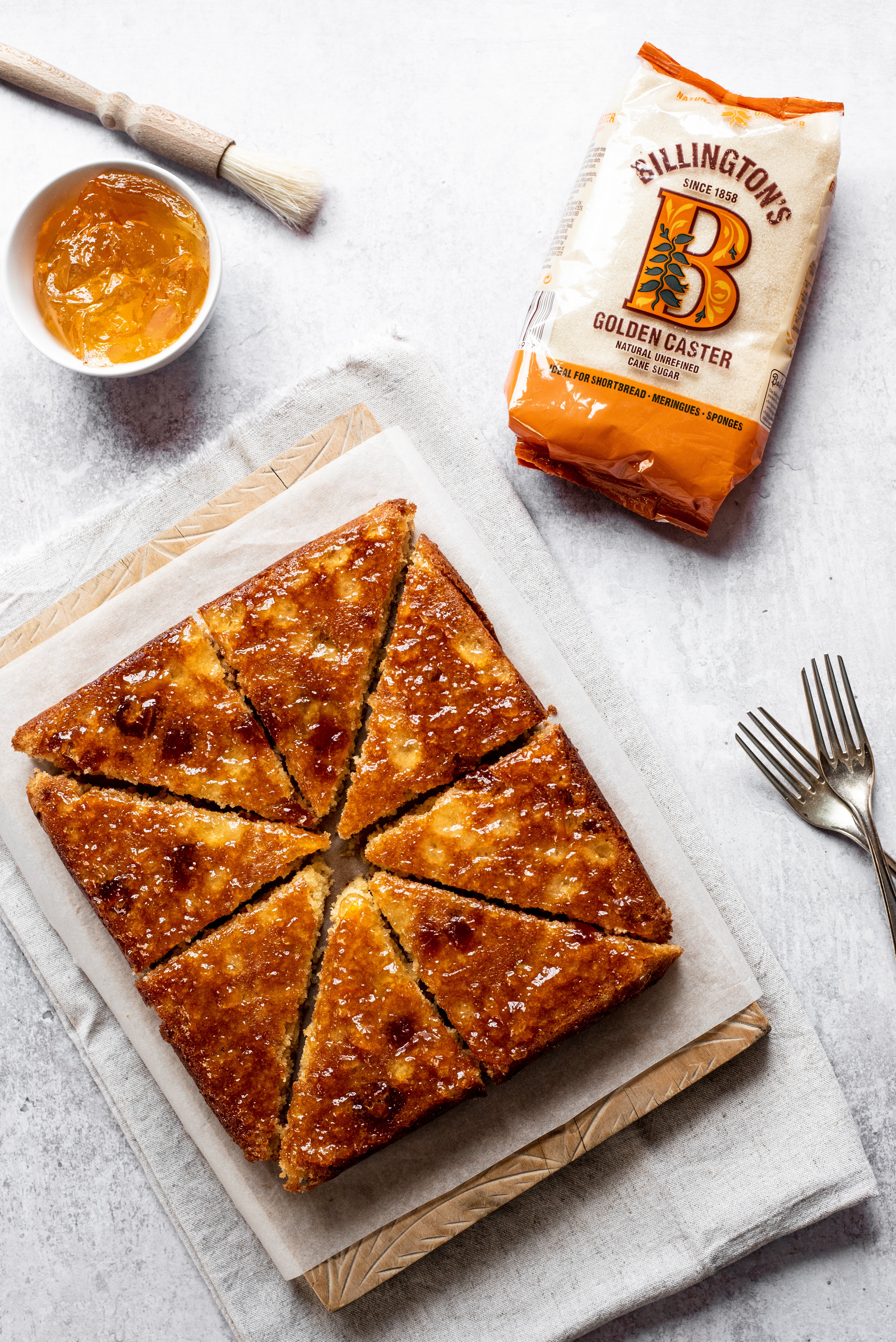 Marmalade Traybake lay on a sheet of baking paper, next to a bag of Billington's Golden Caster sugar and forks