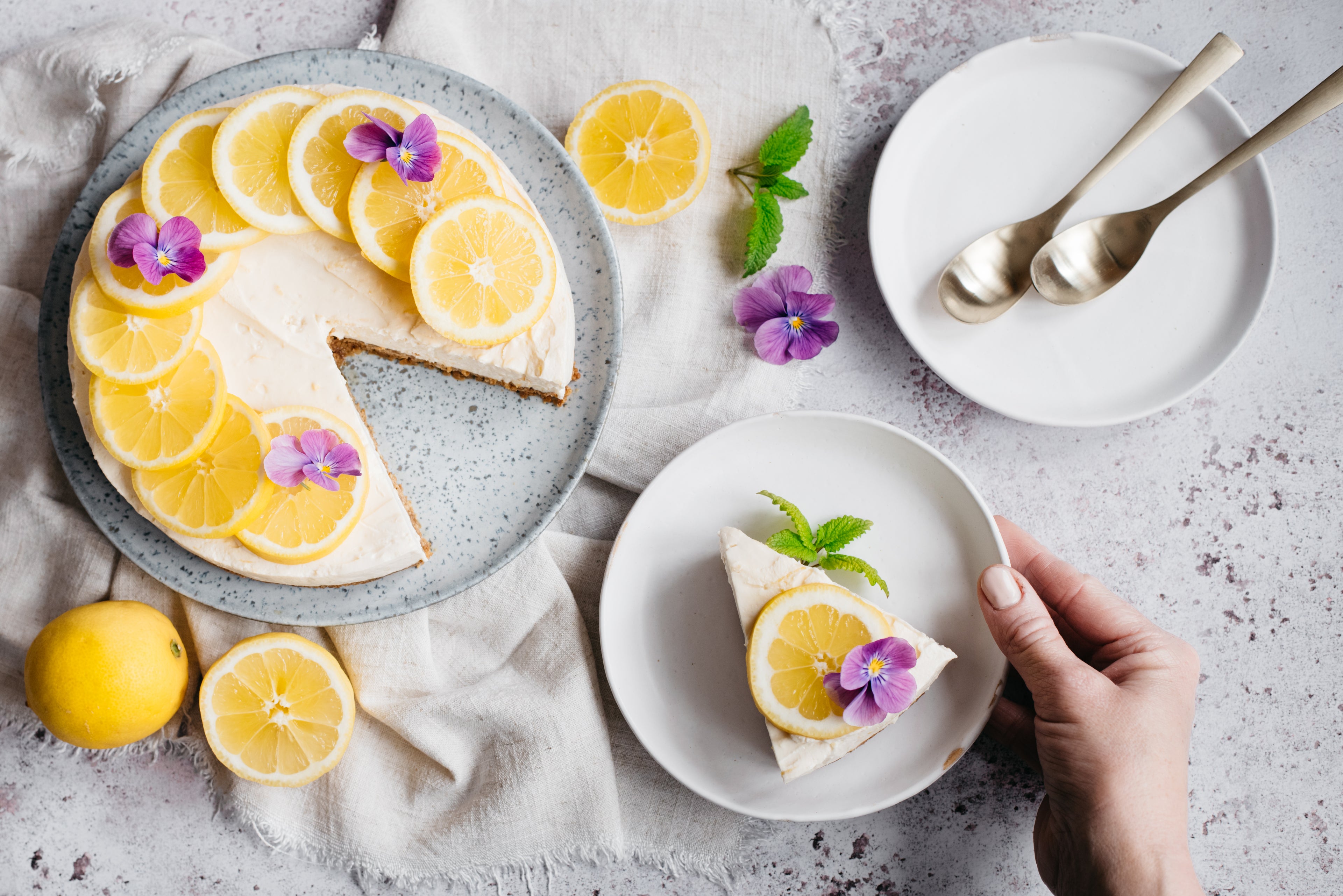 Lemon cheesecake with slice removed, one slice on white plate and plate with spoons