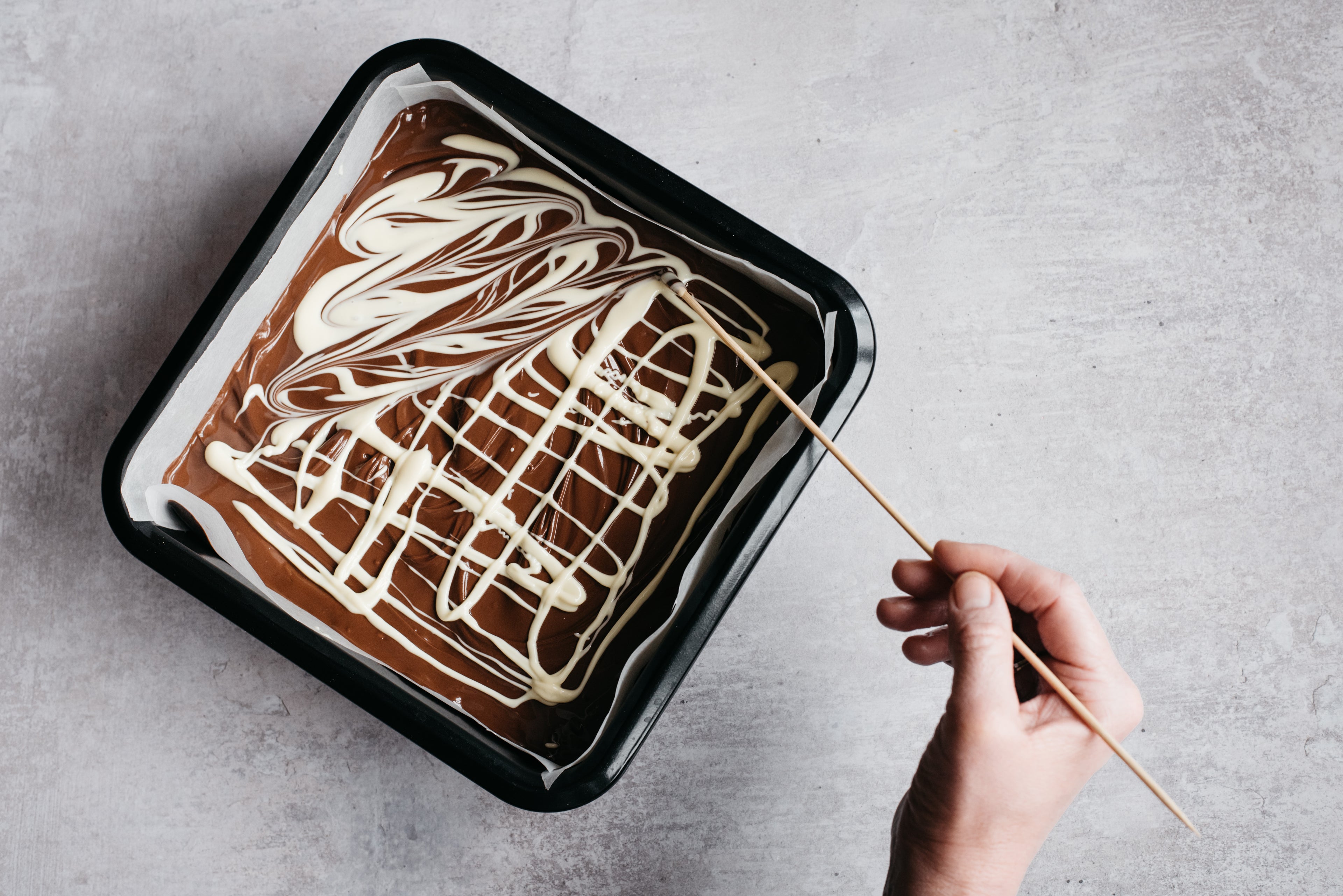 Hand decorating Mars Bar traybake in cake tin with white chocolate and wooden skewer