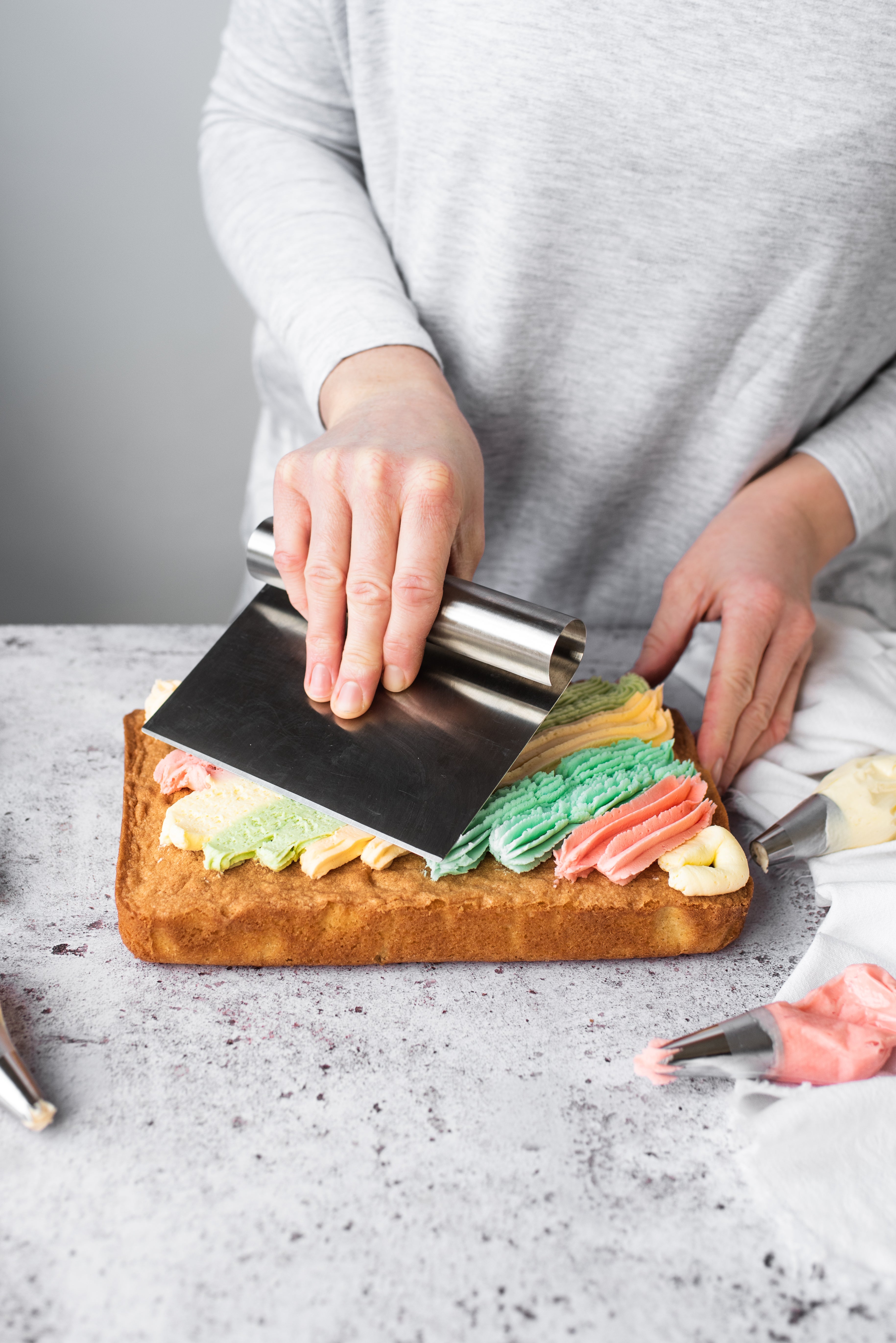 rainbow buttercream being piped onto a traybake cake