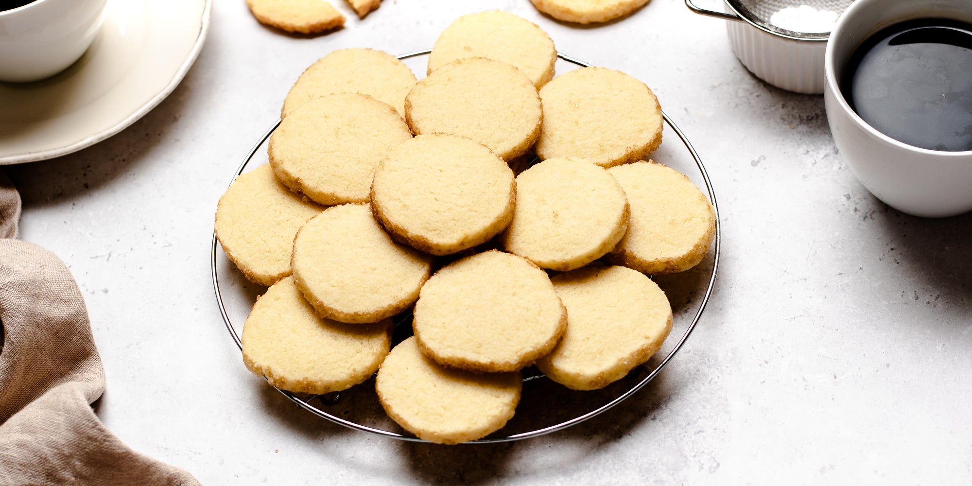 Close-up of a batch of fresh shortbread biscuits on a plate, next to cups filled with coffee