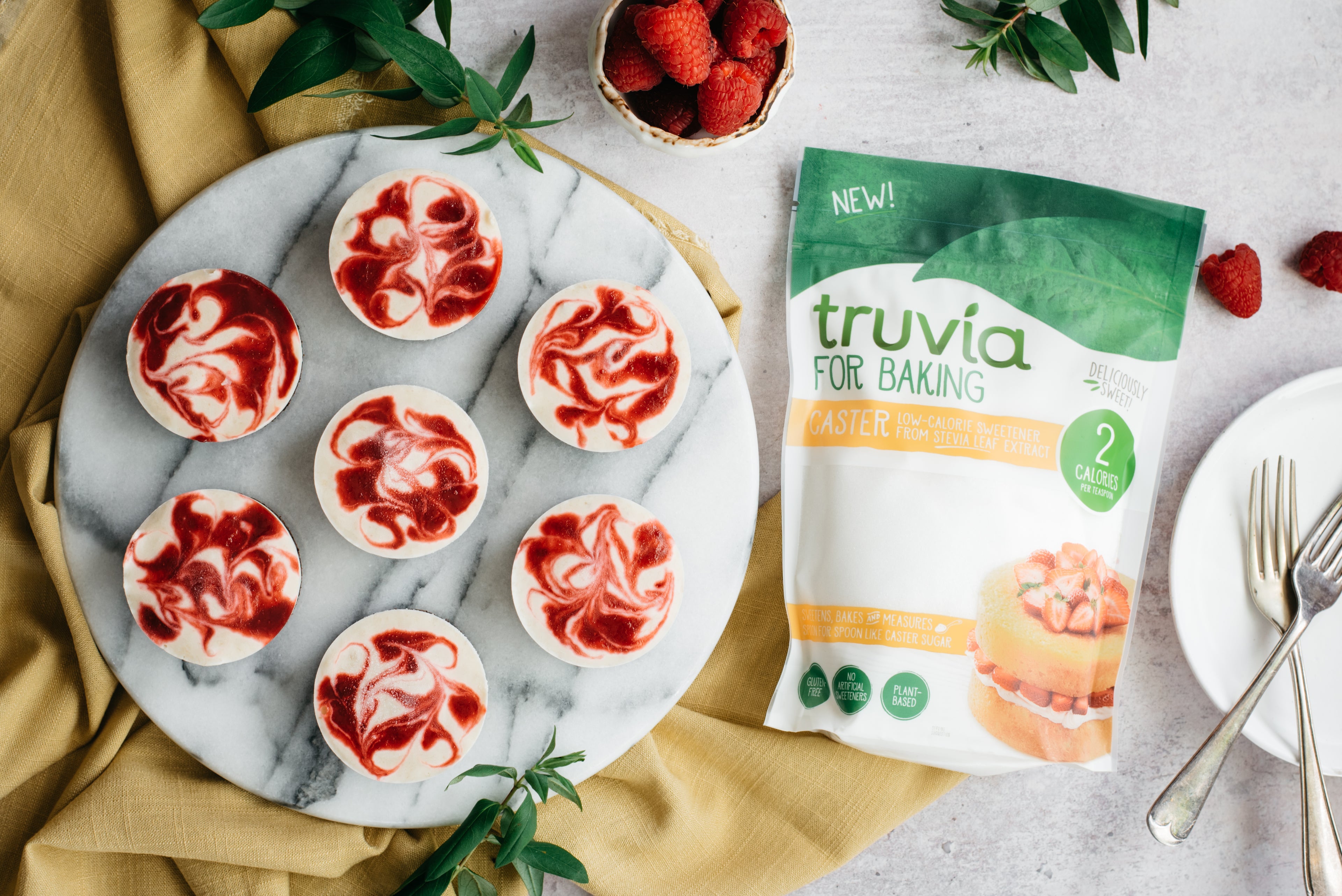 A top down view of a plate of vegan raspberry cheesecake cups next to a pack of truvia for baking caster