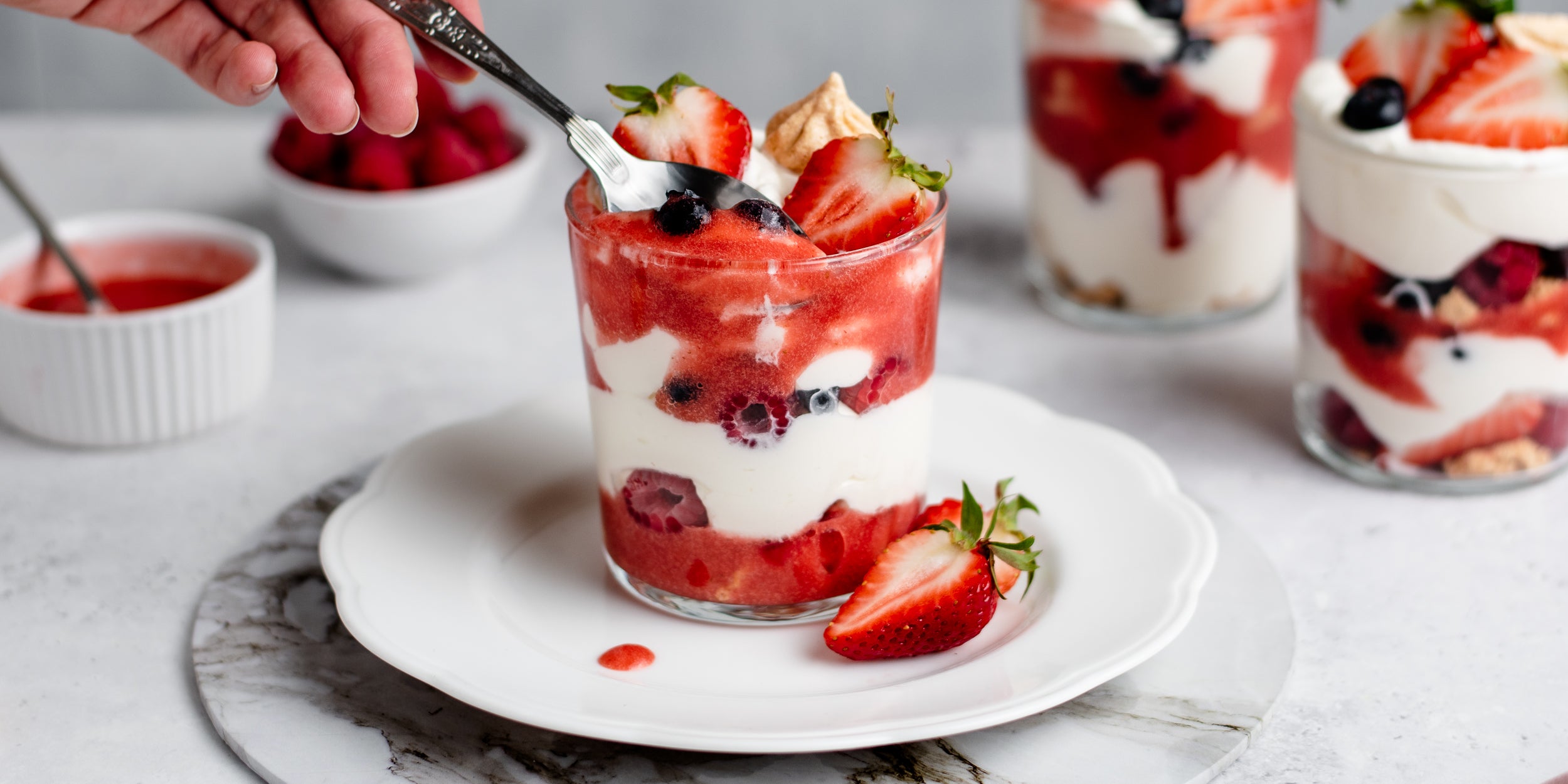 Summer Berry Eton Mess being spooned with strawberry puree and topped with strawberries
