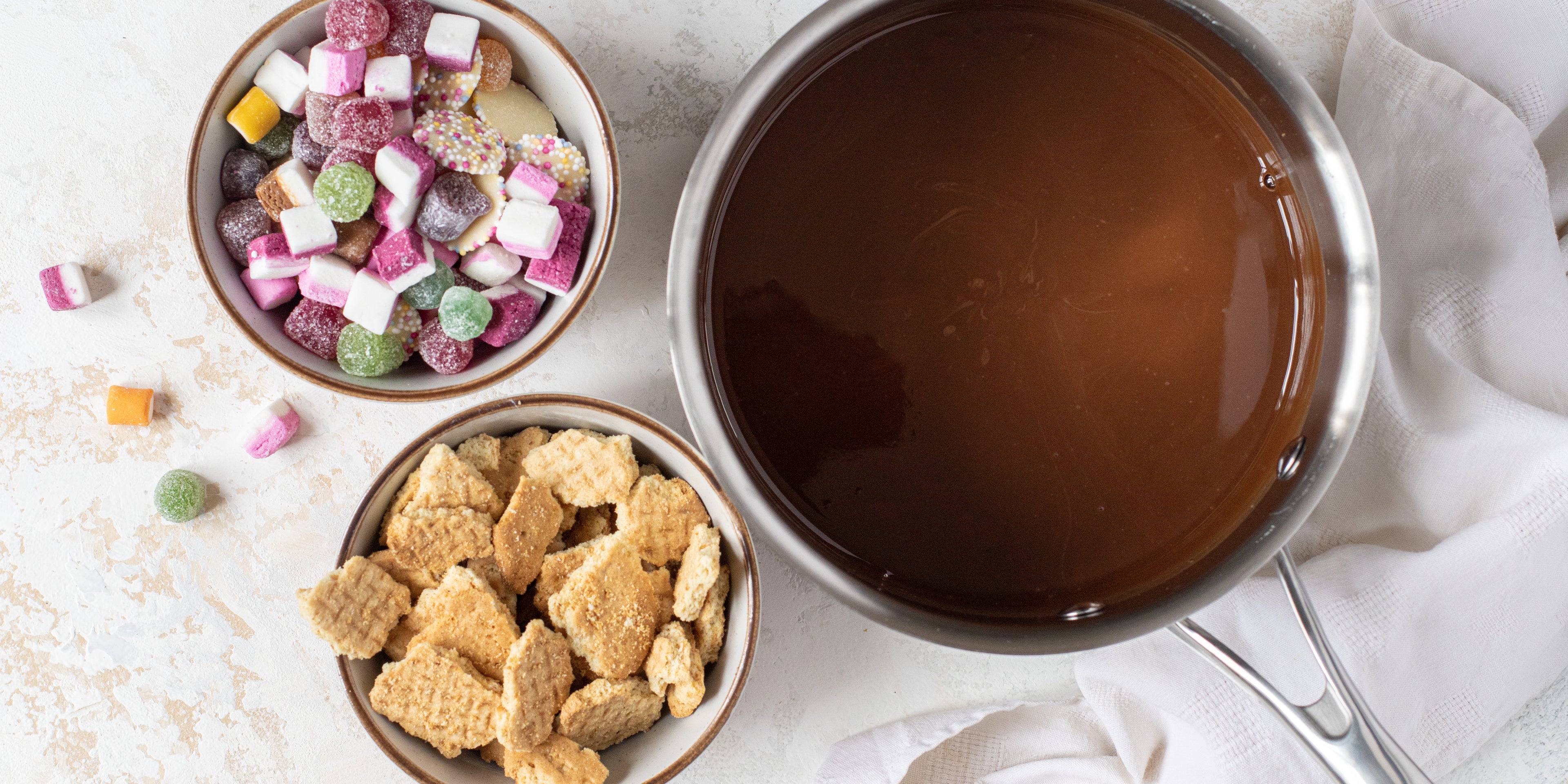 Top view of Sweetie Rocky Road ingredients, with a bowl of crumbled biscuits and a bowl of dolly mixtures