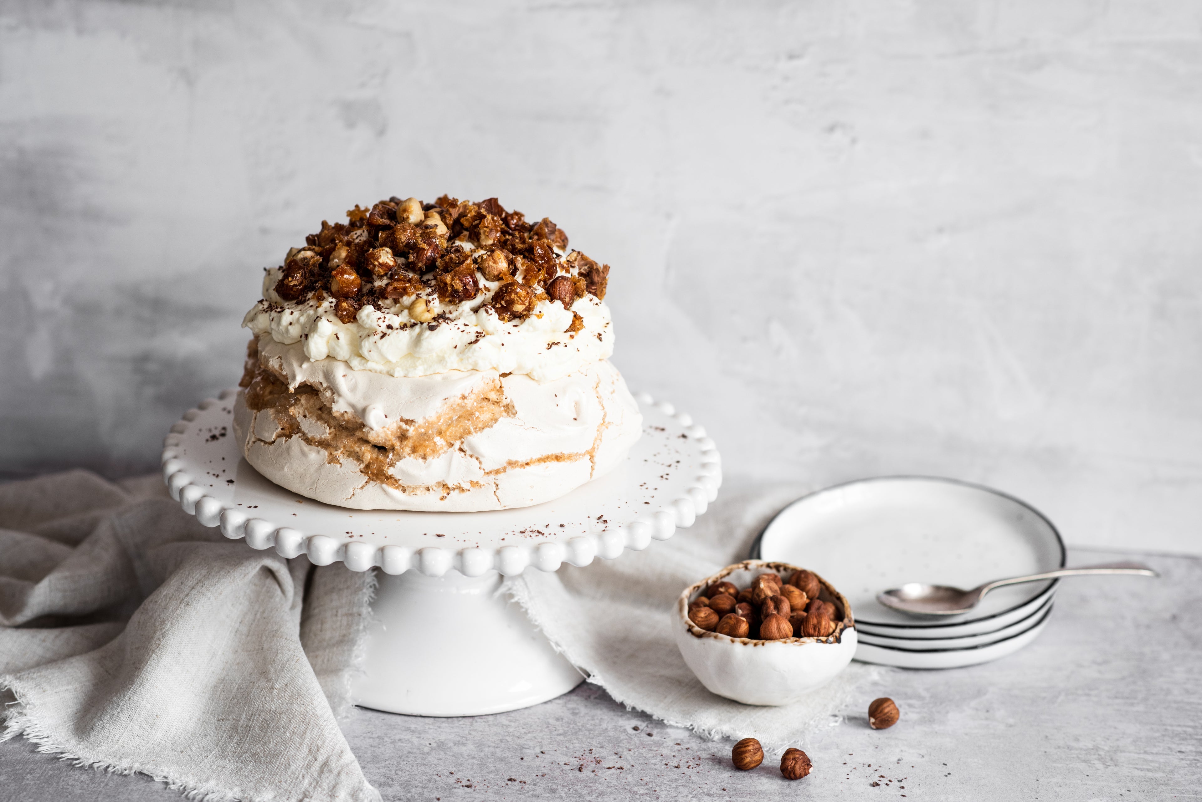 Coffee roasted hazelnut meringue on stand topped with hazelnuts next to a bowl of hazelnuts