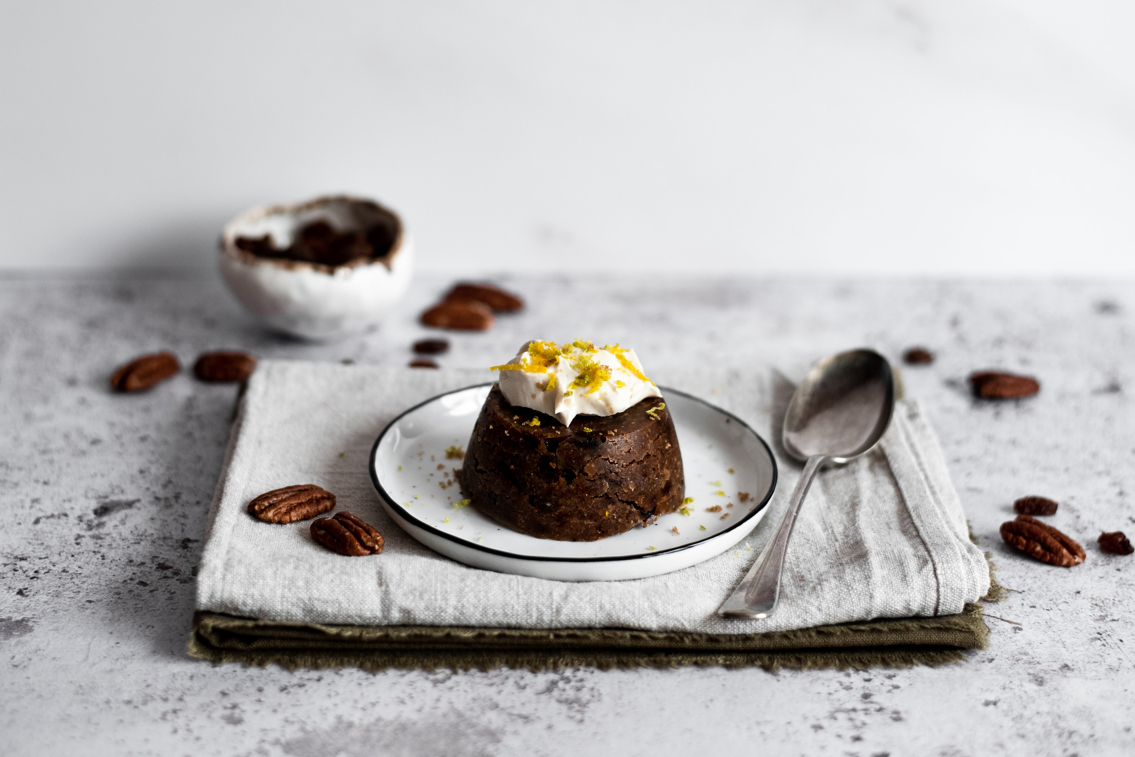 Close up of mini christmas pudding on a plate with a bowl and pecans