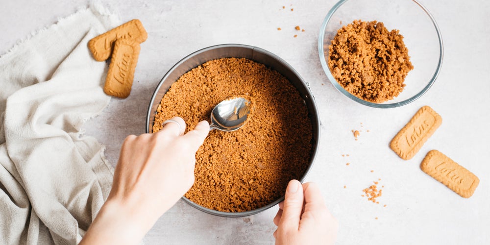 Hand pushing biscoff crumbs into the base of the tin