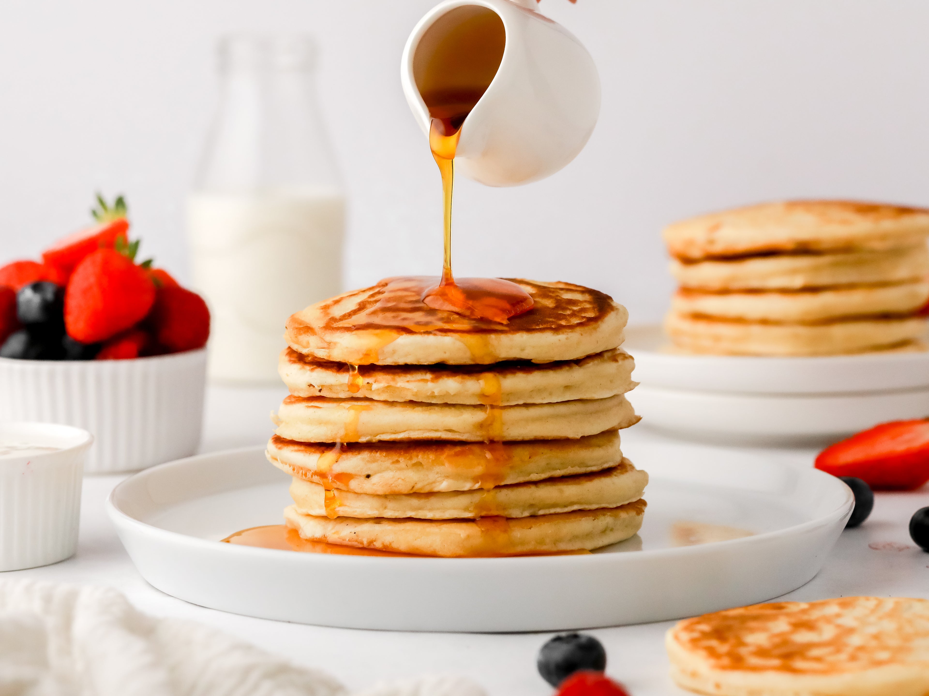 Syrup being poured on top of a stack of pancakes