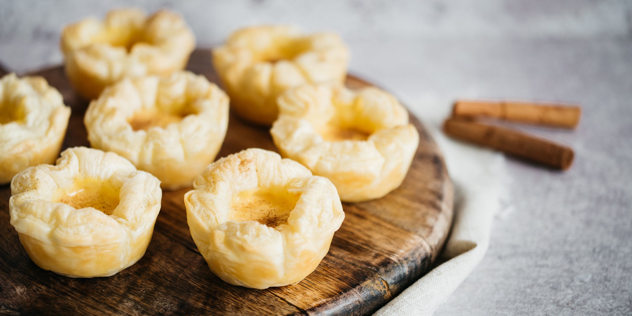 Close up of portuguese custard tarts on a wooden board with cinnamon sticks beside