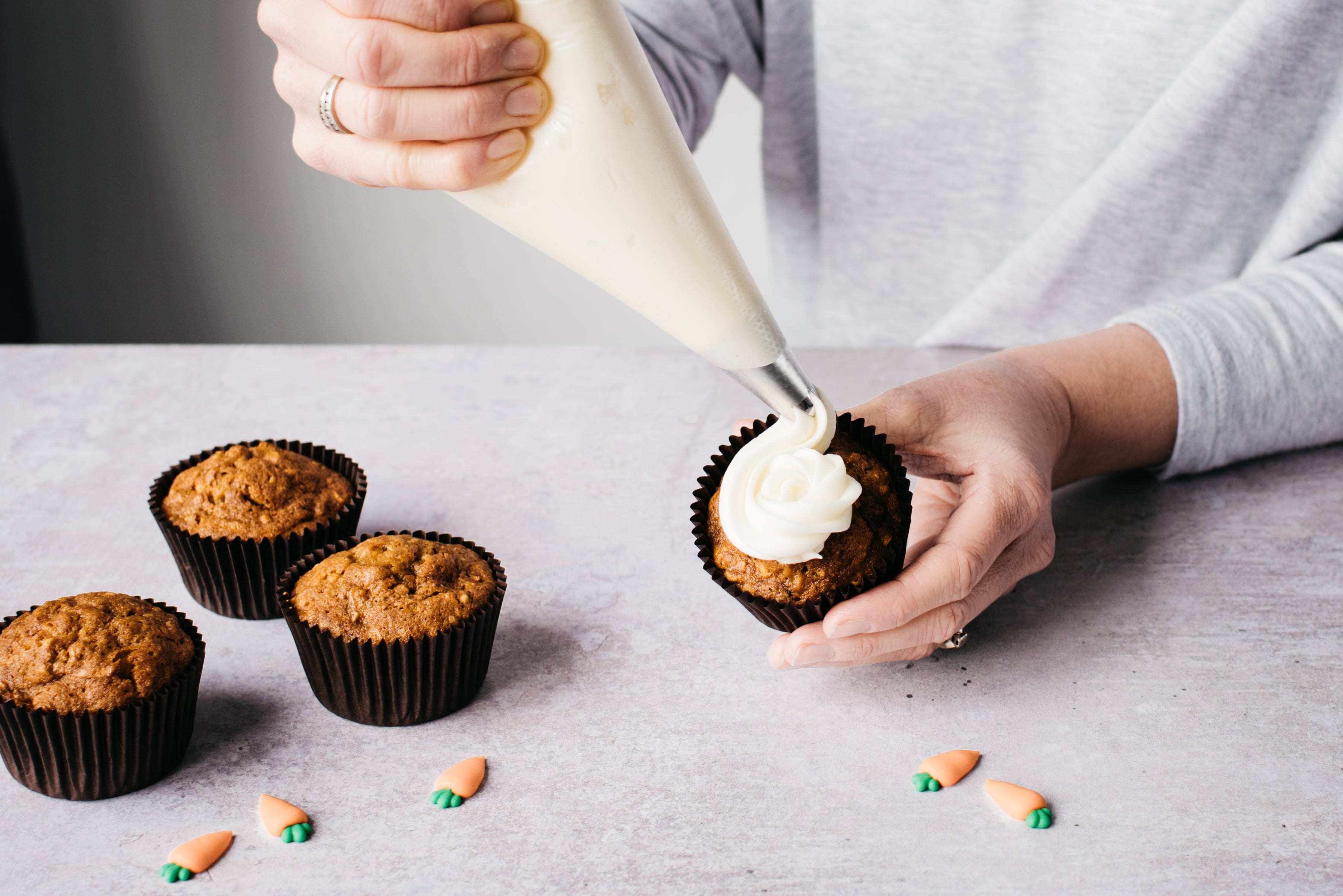 Carrot cake cupcakes being topped with cream cheese frosting from a piping bag