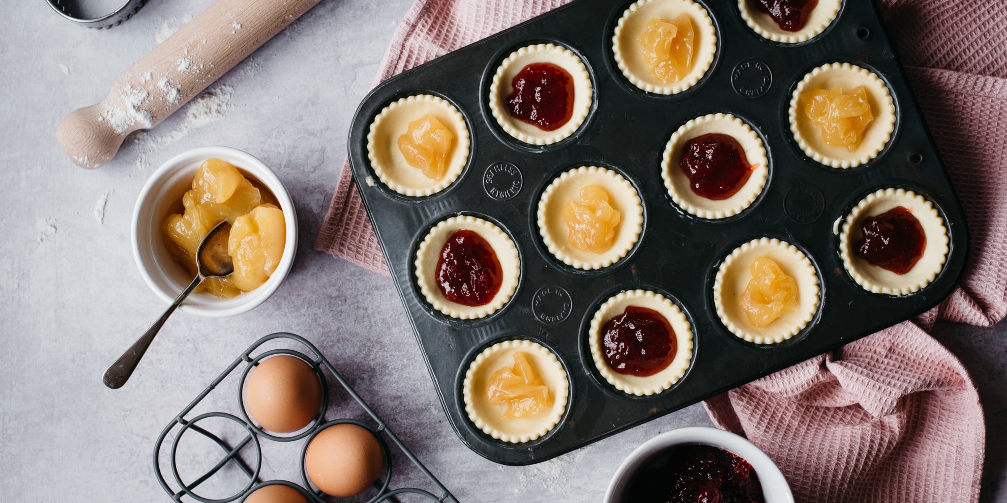 Strawberry & Apricot Jam Tarts in a baking tray being filled with jam ready to bake