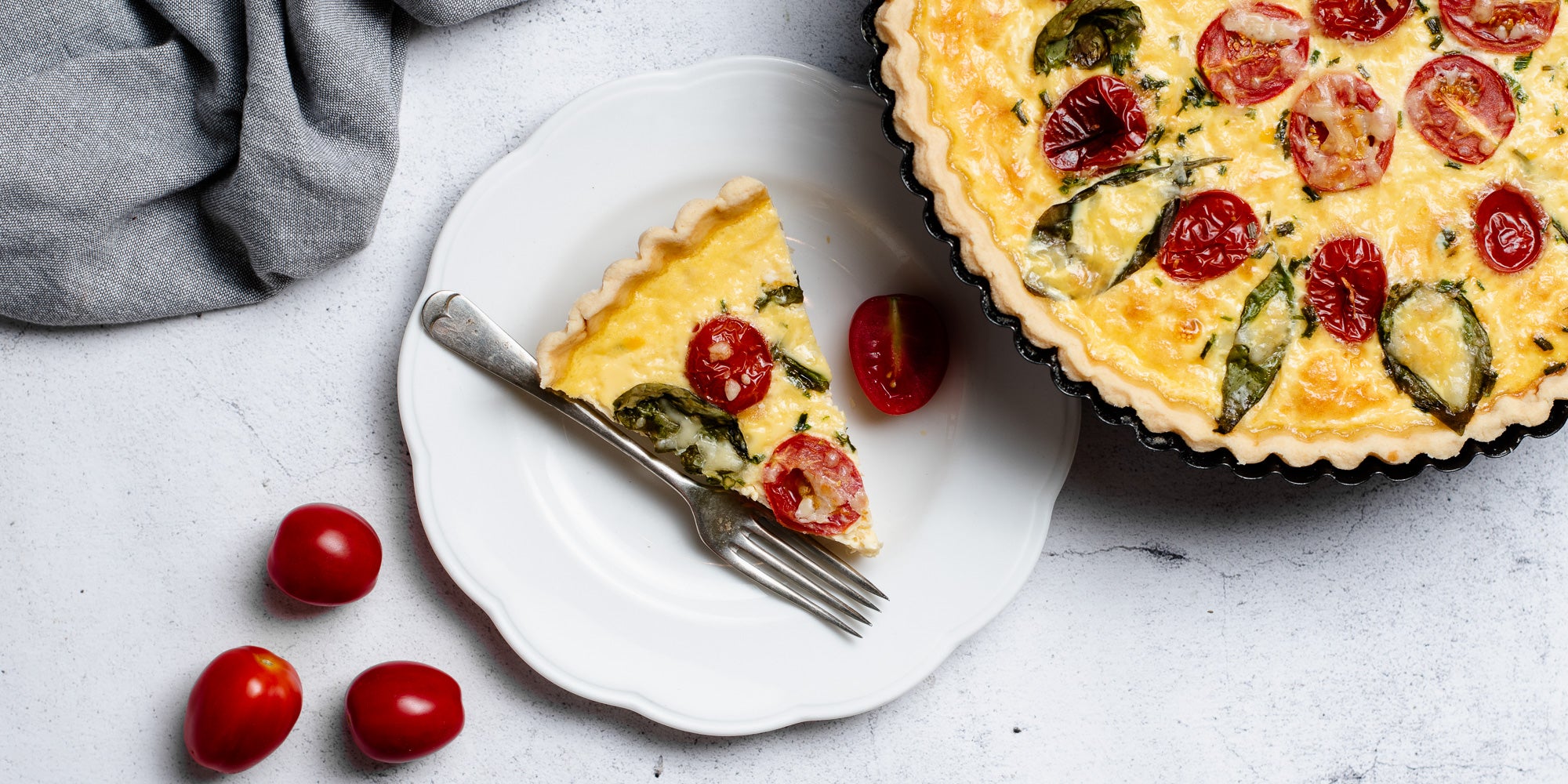 Cheese & Tomato Quiche with a slice on a plate with a fork, next to some chopped tomatoes