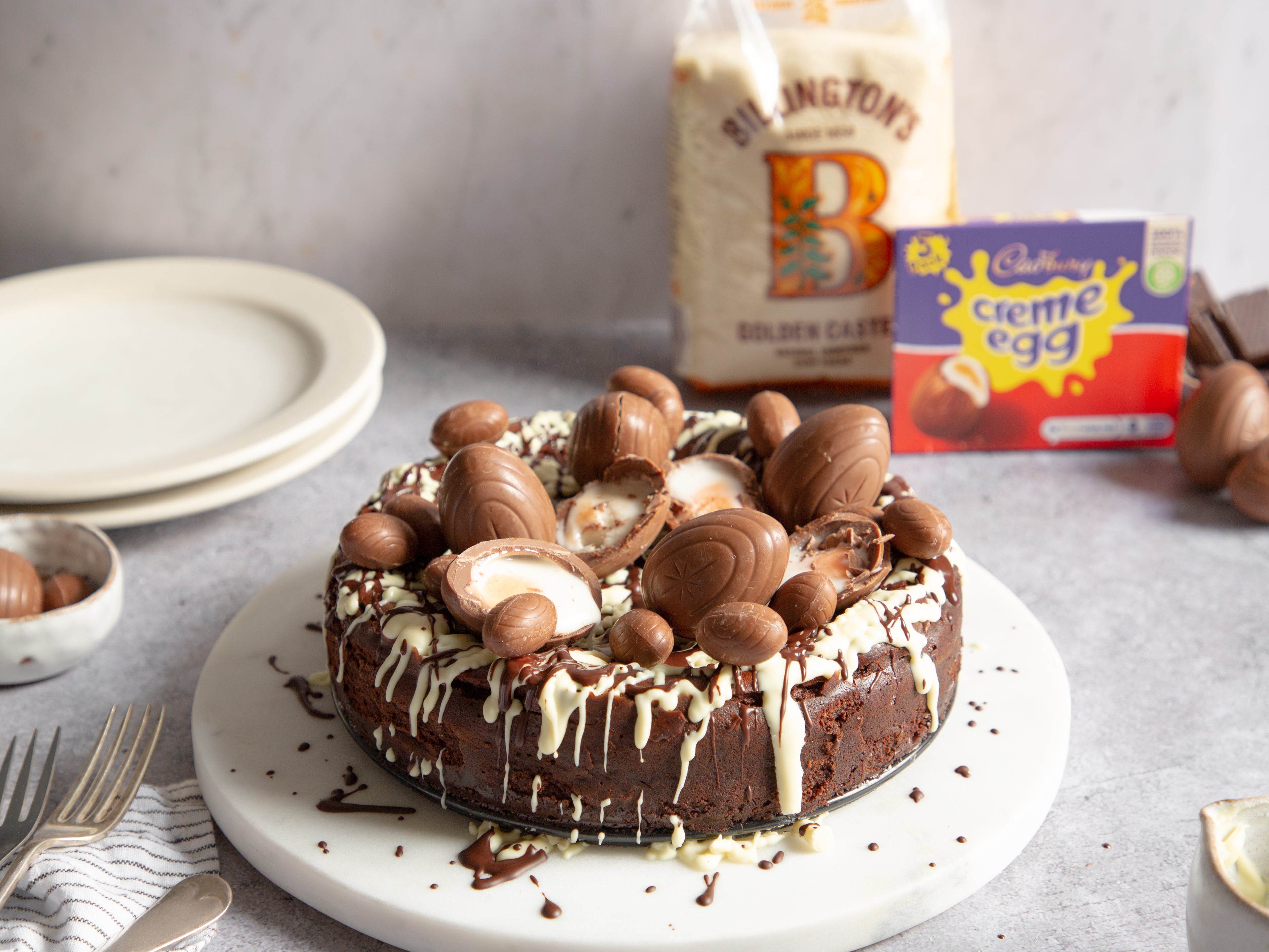 Chocolate Cheesecake topped with Creme Eggs, white chocolate drizzle with a pack of Billington's Golden Caster in the background