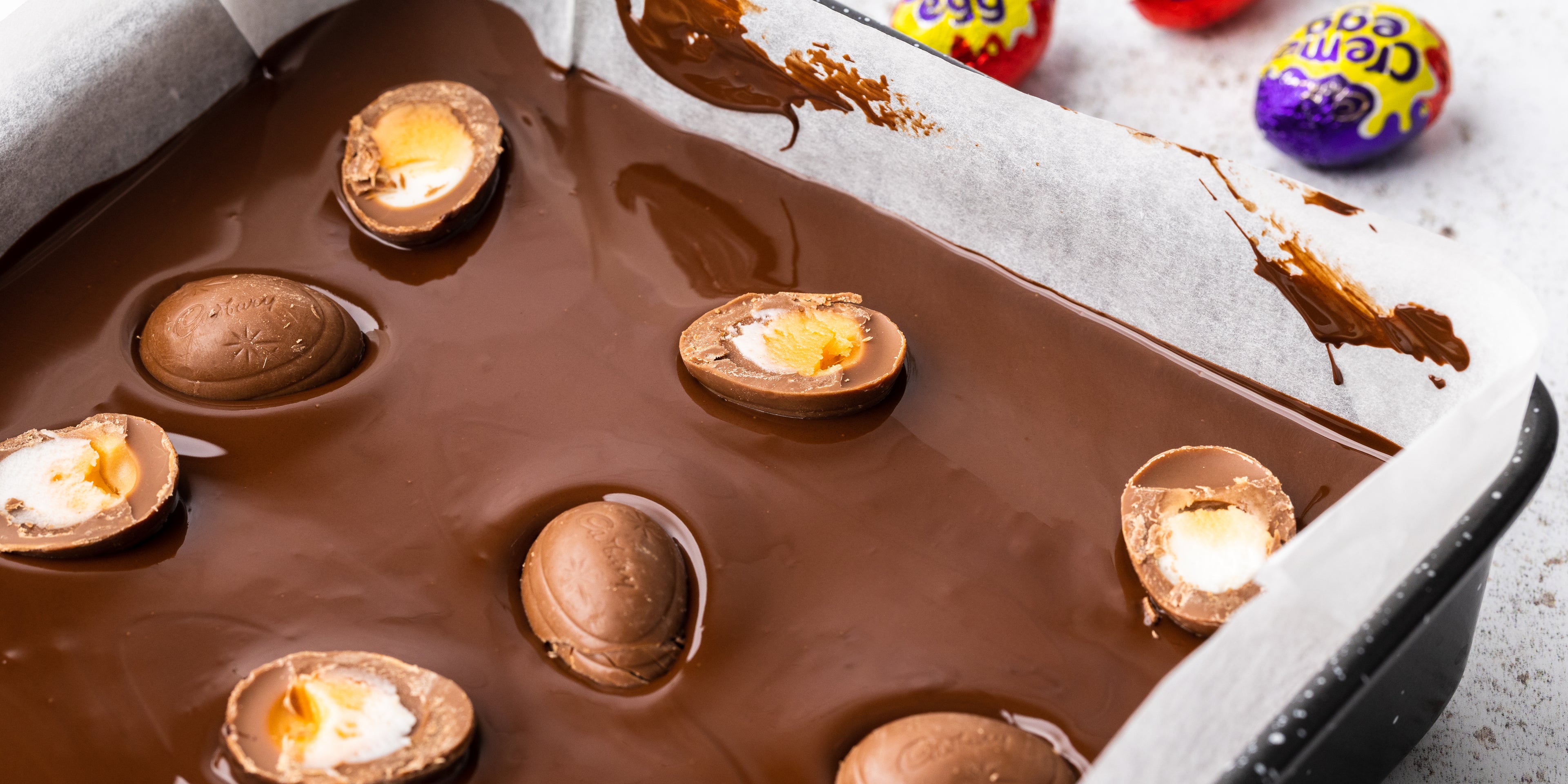 Creme eggs on top of melted chocolate in a square baking tin