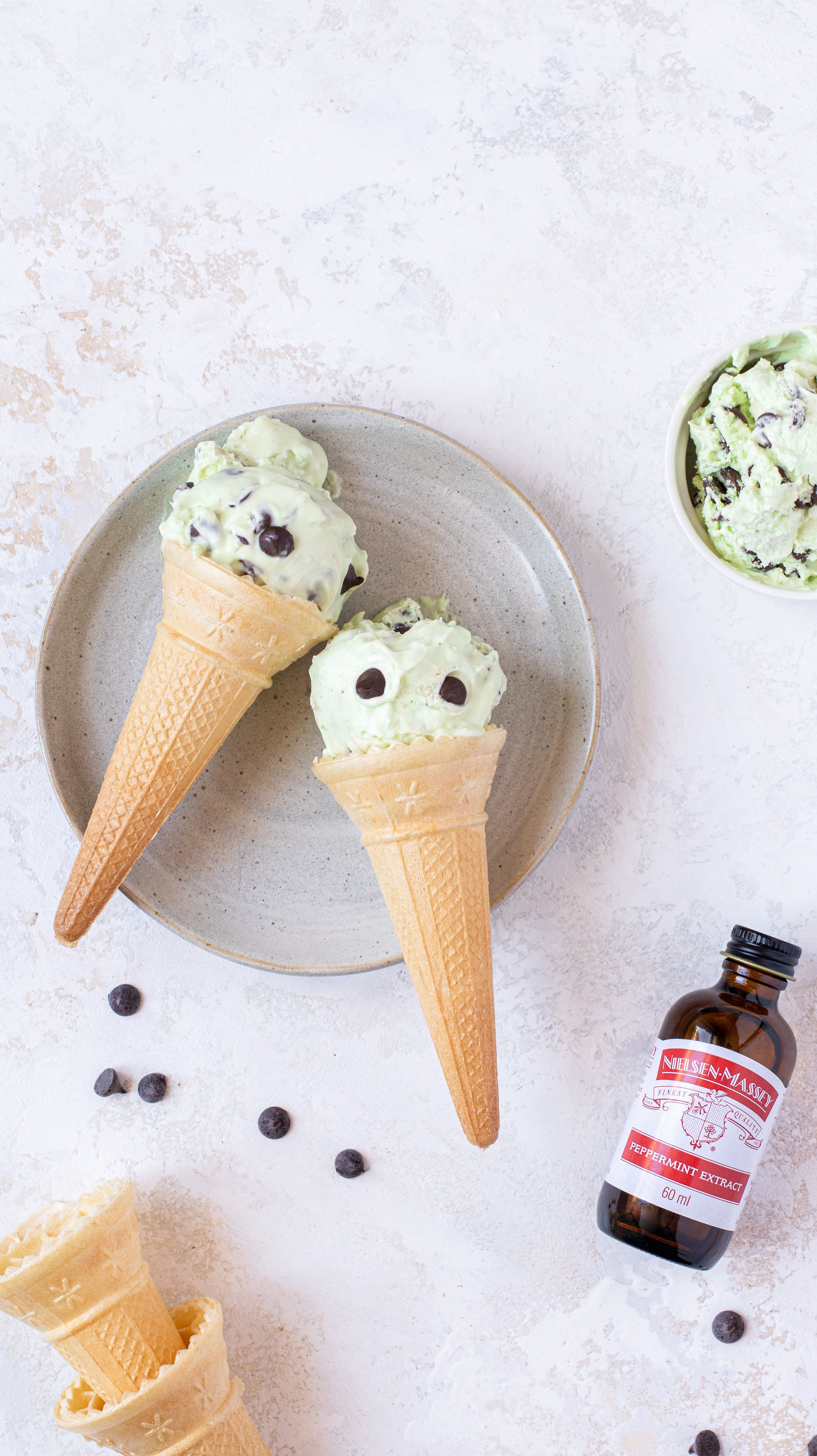 Mint chocolate chip ice cream in a cone on a plate with cones and peppermint extract