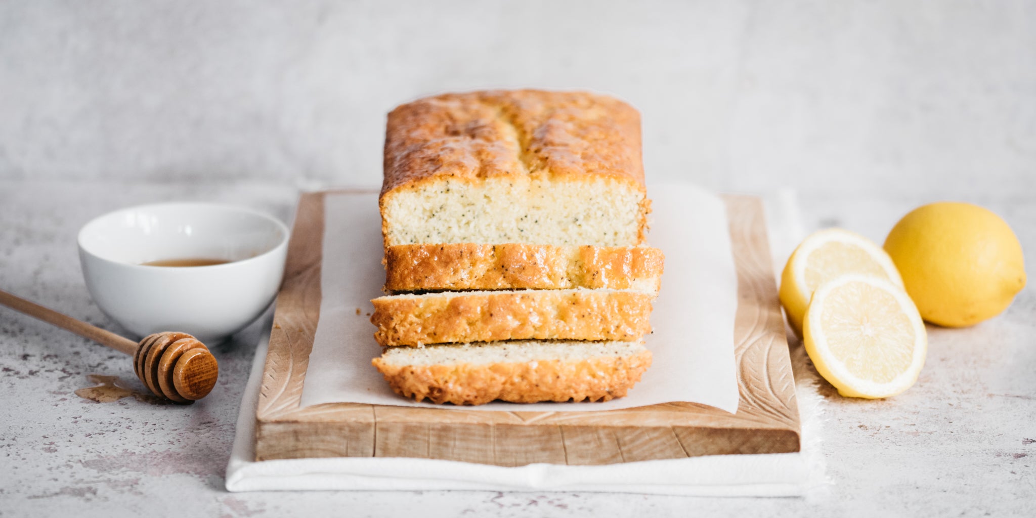 Lemon loaf on a chopping board with a bowl of honey beside and some chopped lemons