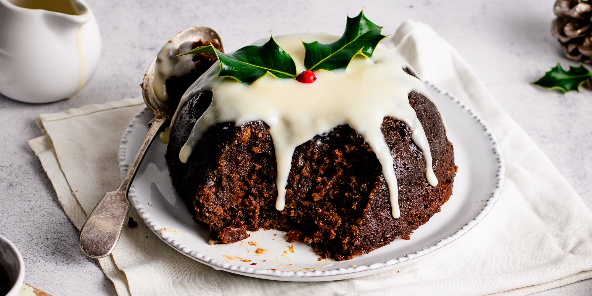 Close up of Last Minute Christmas Pudding drizzled with cream or brandy butter, with a decorative piece of holly ontop
