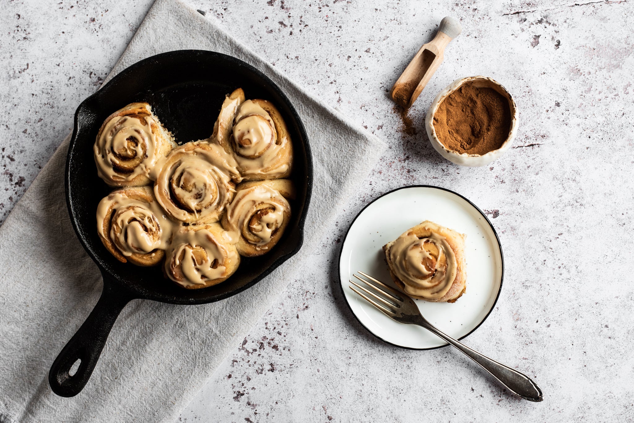Cinnamon rolls in a skillet with one removed and on a white plate infront with a fork
