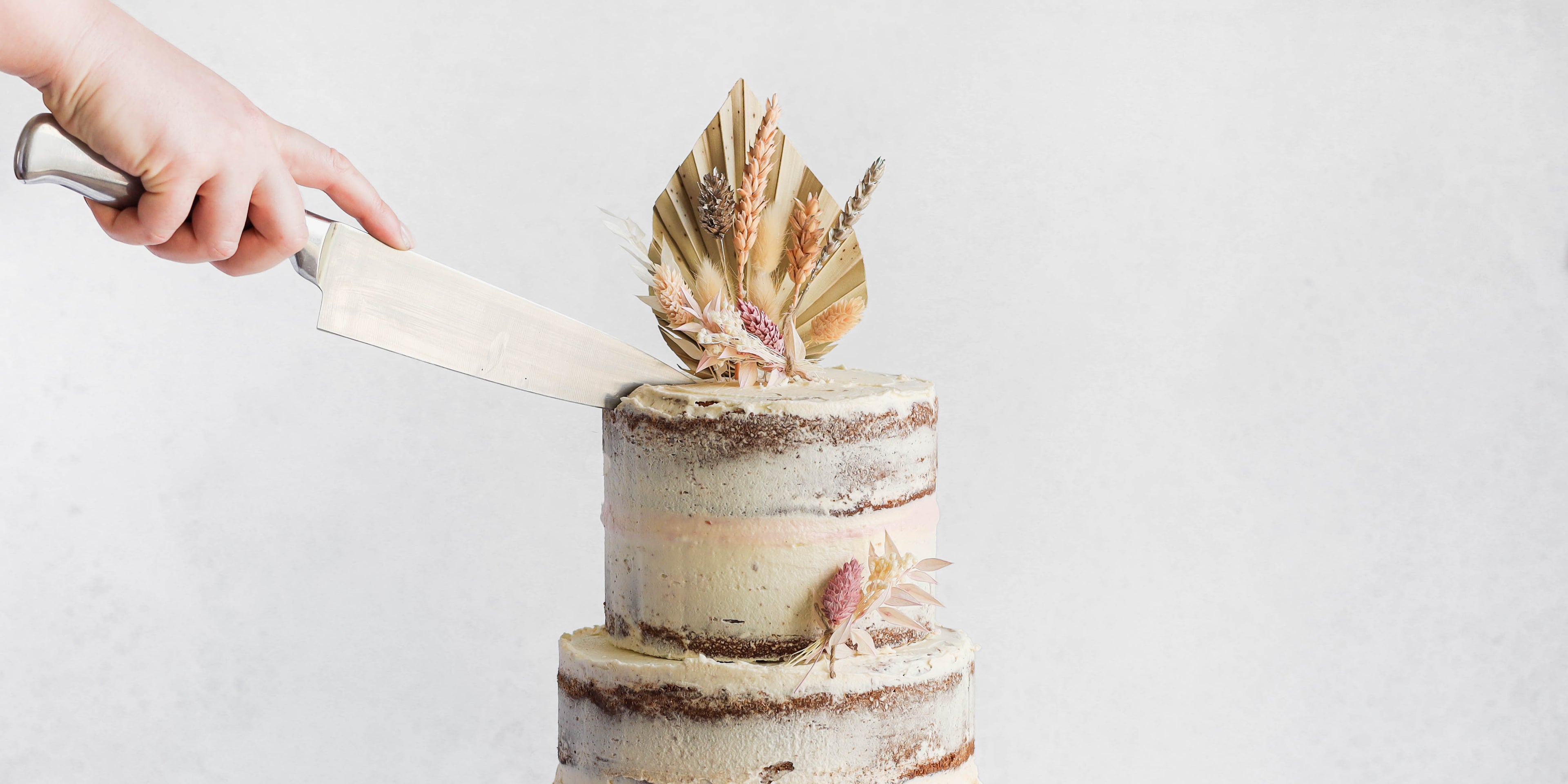 Side view of a knife slicing into a naked vanilla celebration cake