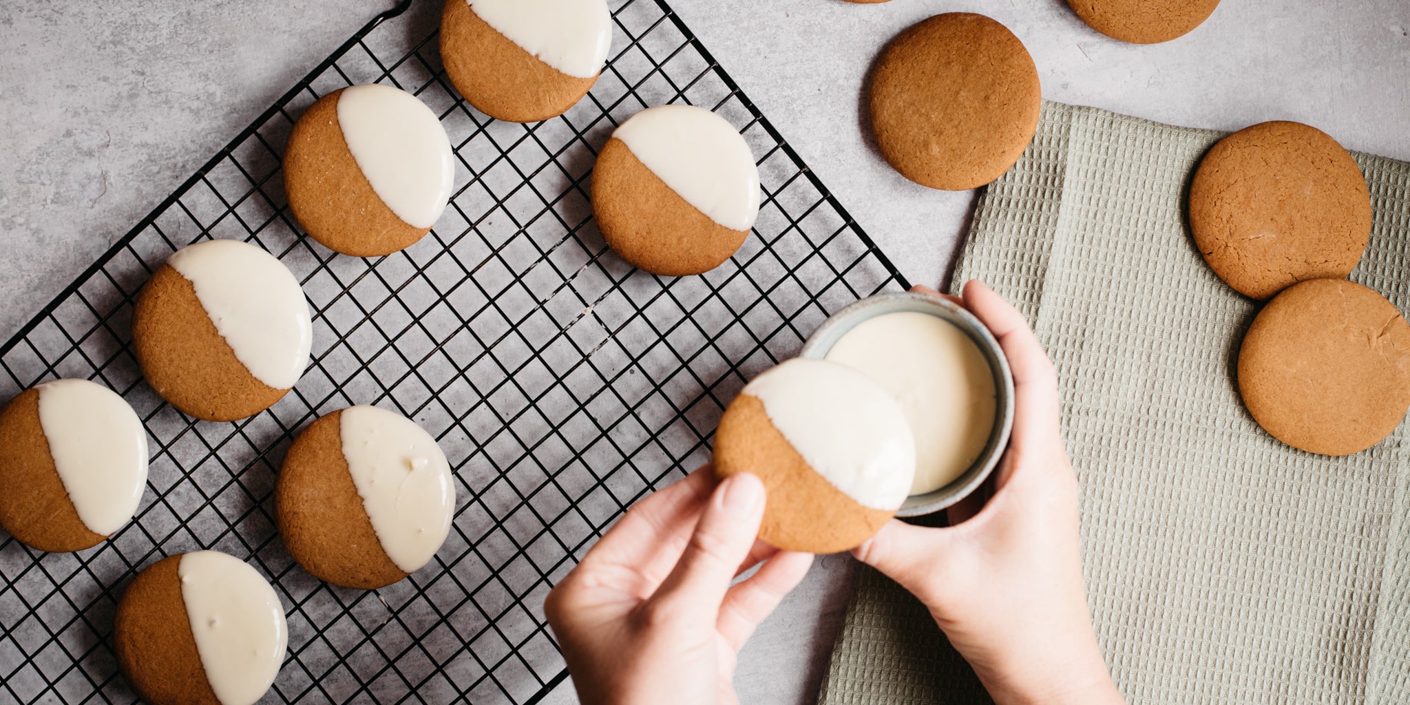 Citrus Gingerbread Cookies being hand dipped in white chocolate with a hand, and left to set on a wire rack,