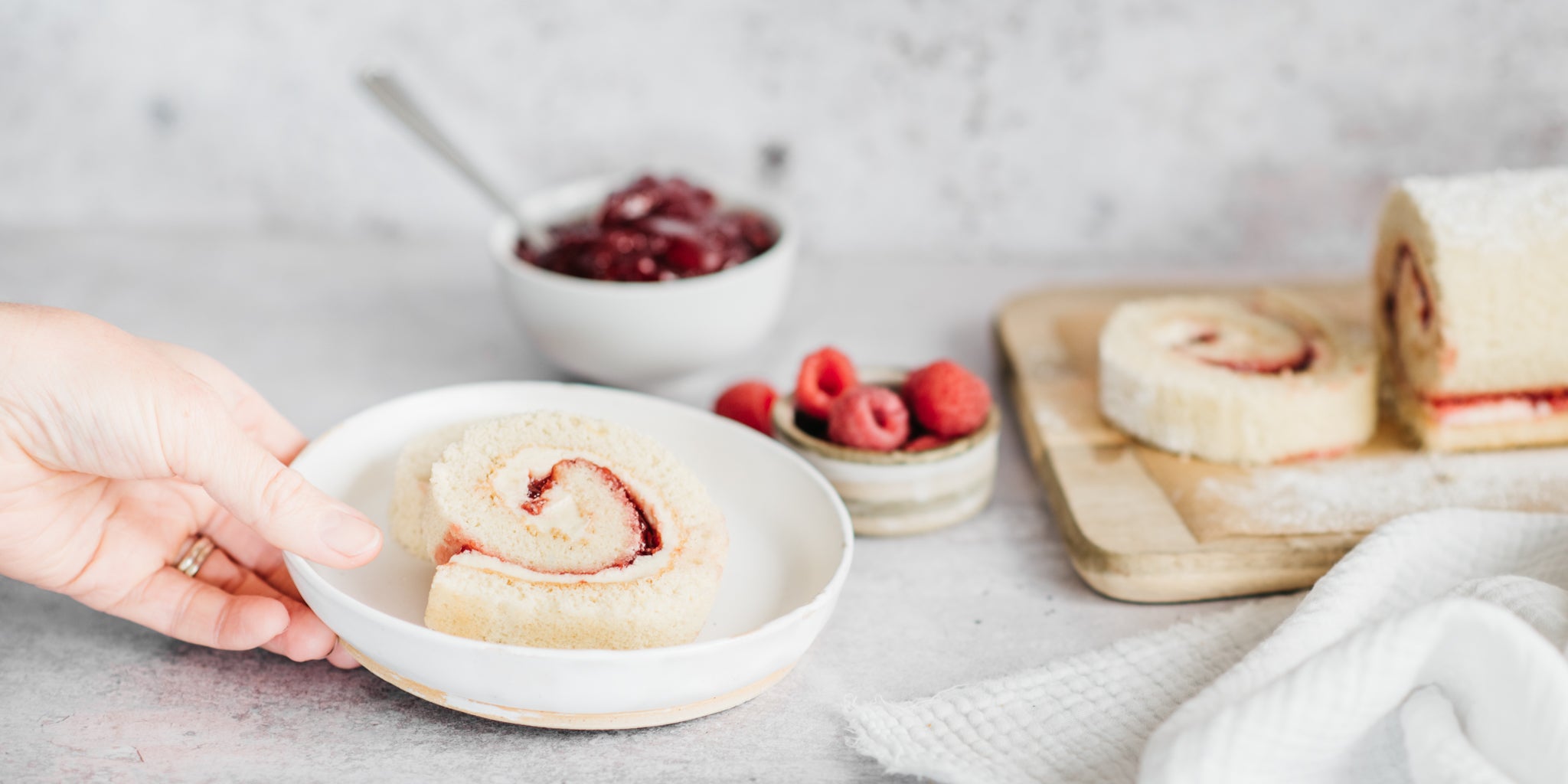 A hand reaching in the shot to pick up a bowl filled with two slices of vanilla swiss roll