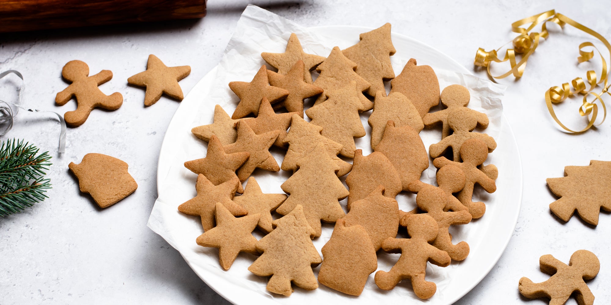 A batch of gingerbread cookies baked from Gingerbread Dough, next to gold ribbon and pine leaves
