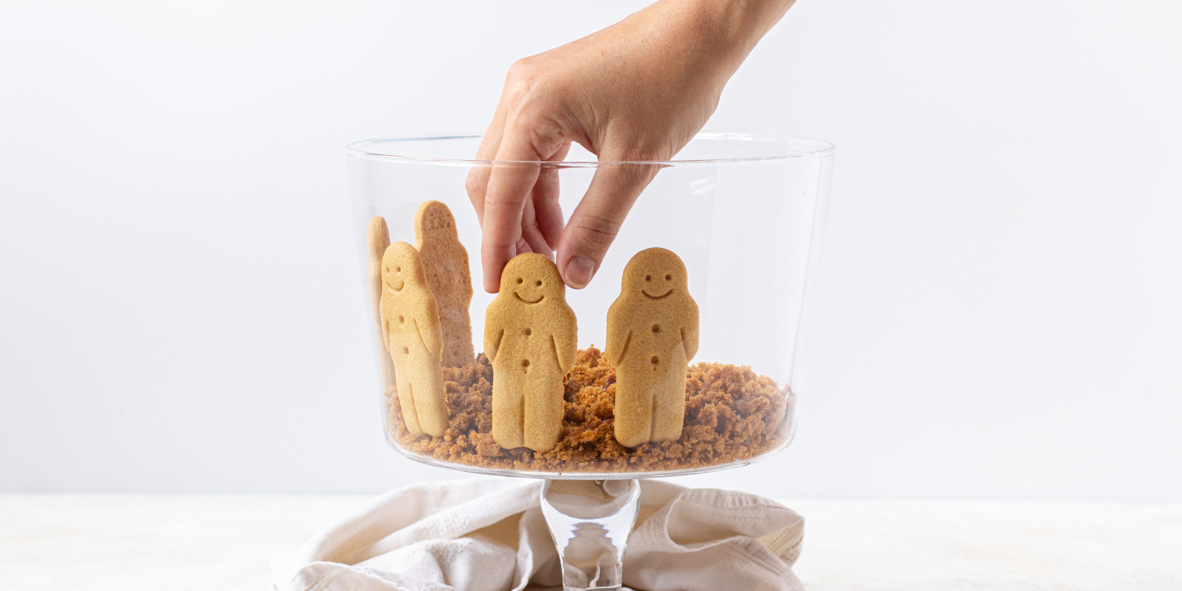 Hand decorating a Gingerbread Trifle with gingerbread men placed around the edge of the glass trifle bowl