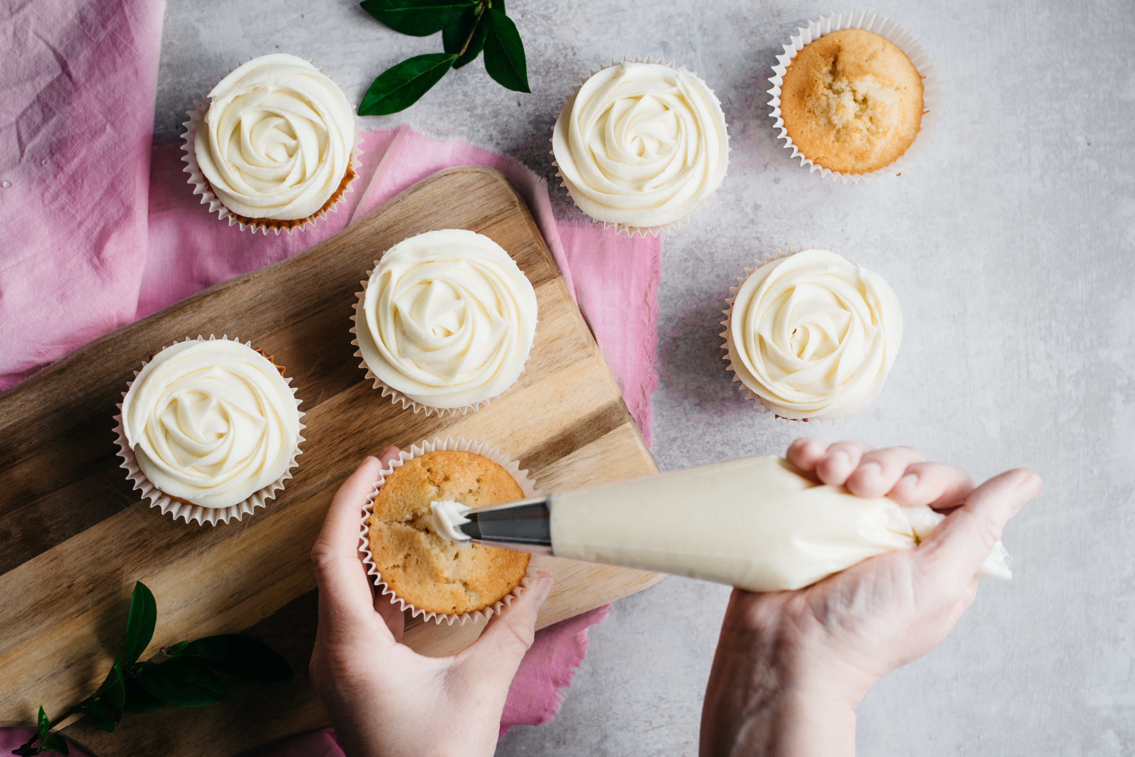 Top down view of a hand piping cream cheese frosting onto a cupcake