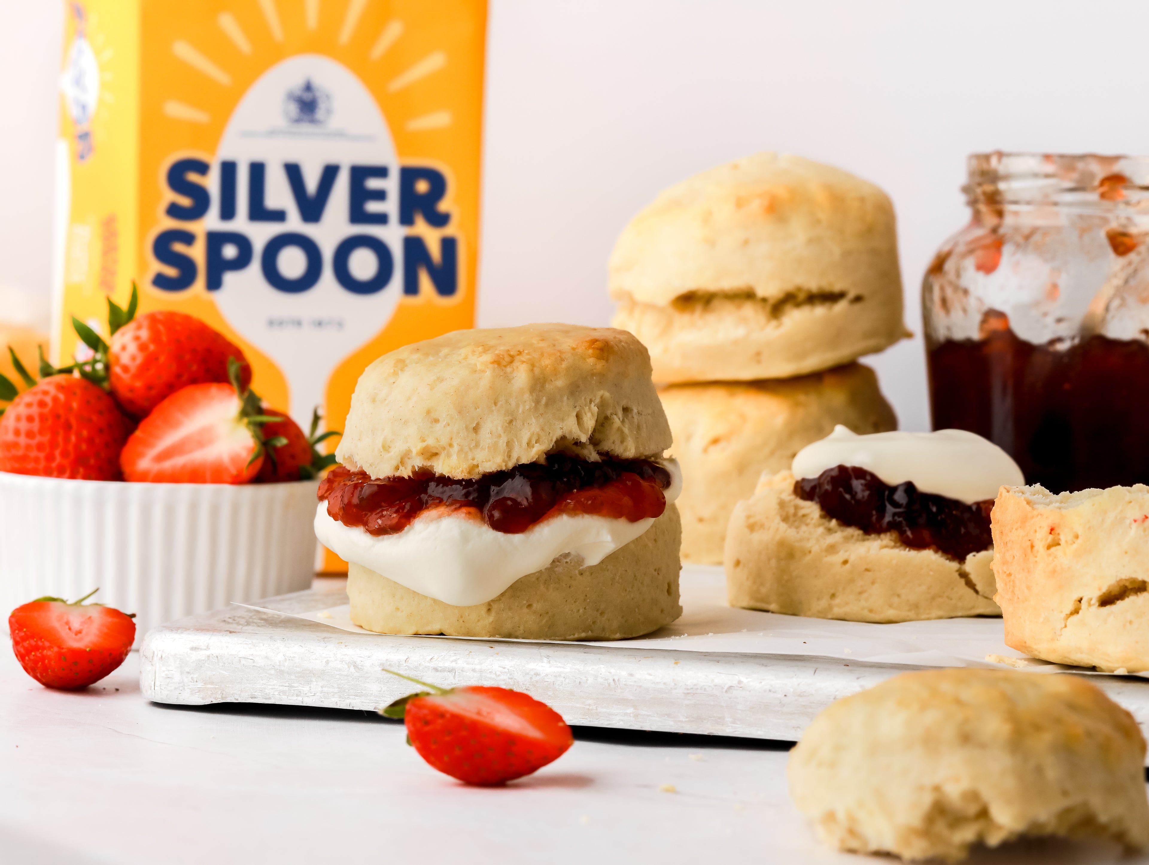 Scone filled with jam and cream and surrounded by a jam jar and strawberries