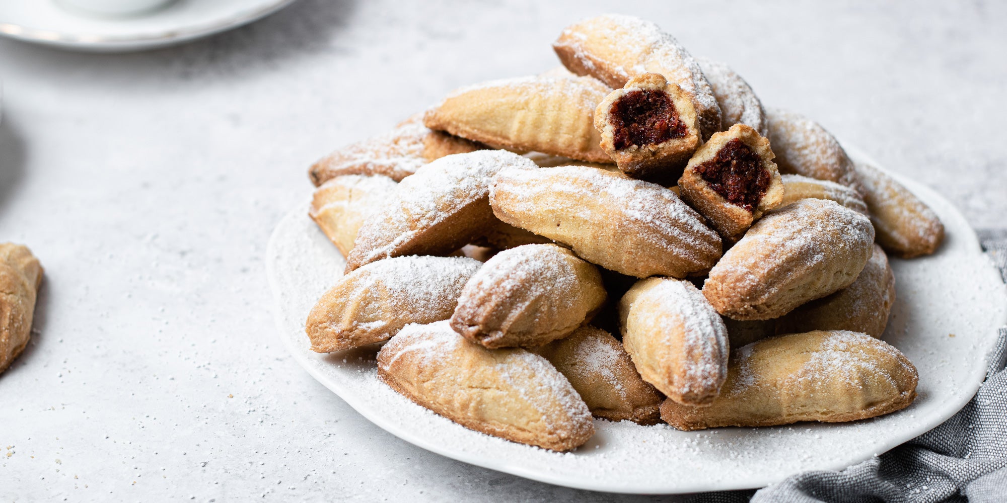 Mamoul cookies stacked on a white plate, with one broken in two and dusted with icing sugar