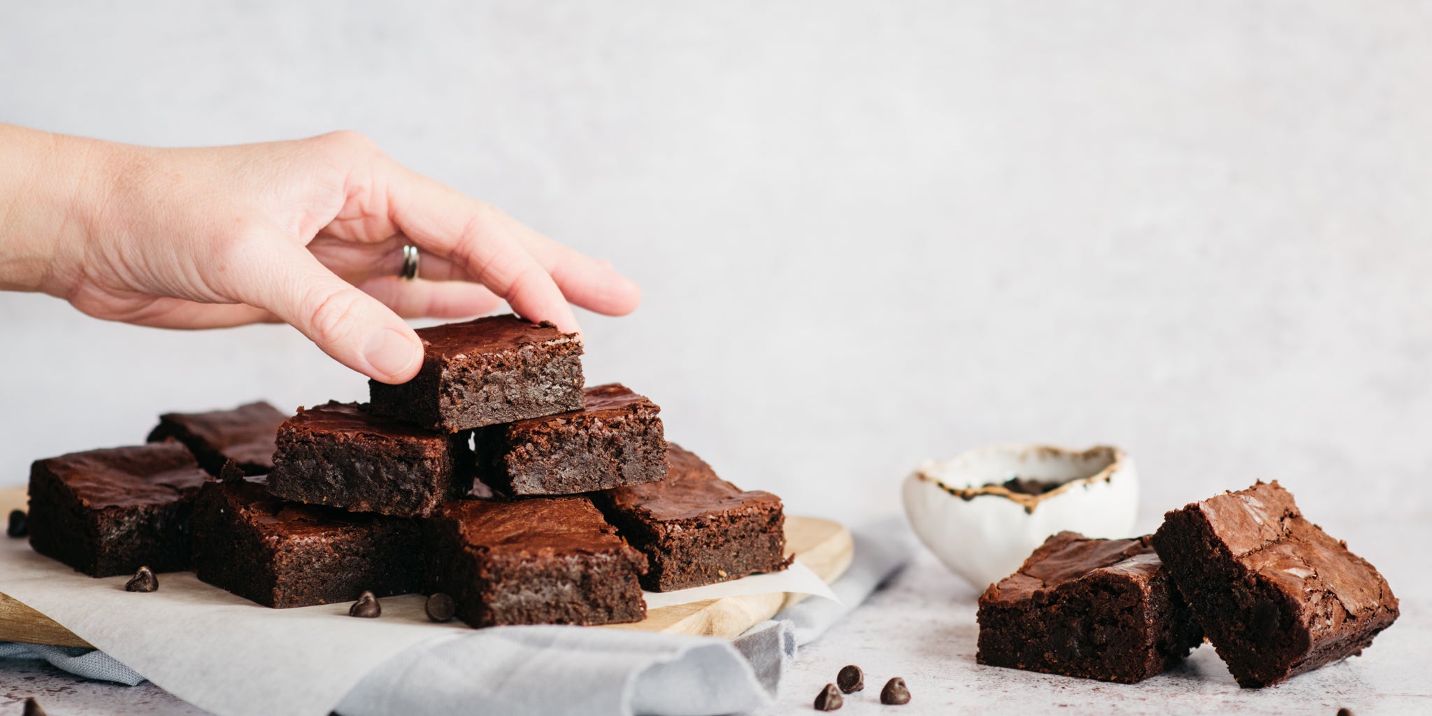 Hand reaching for a Wholemeal Chocolate Brownie, from a stack of a fresh batch of Wholemeal Chocolate Brownies