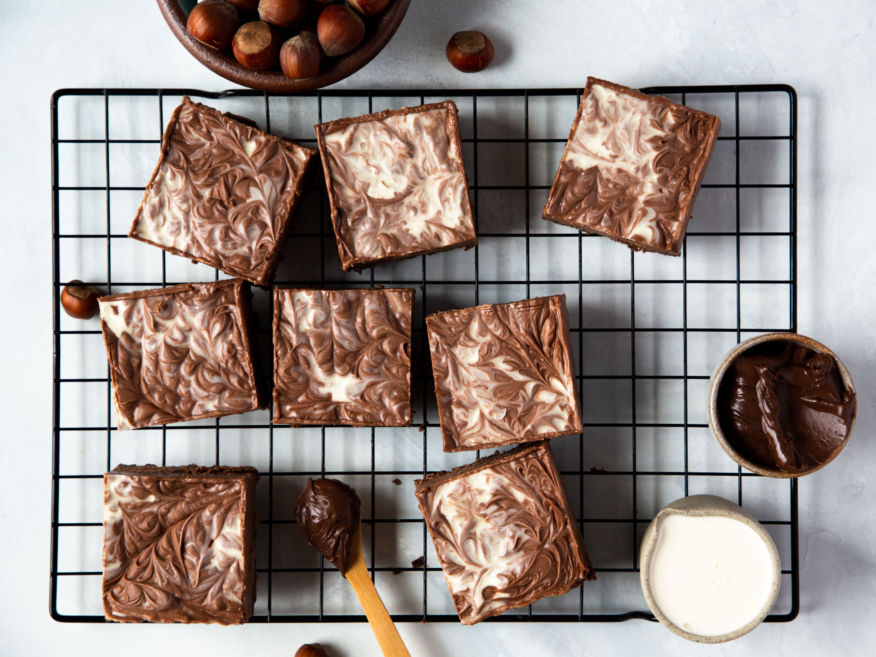 Top view of Nutella Cheesecake Bars on a wire rack, next to a pot of Nutella and a jug of milk