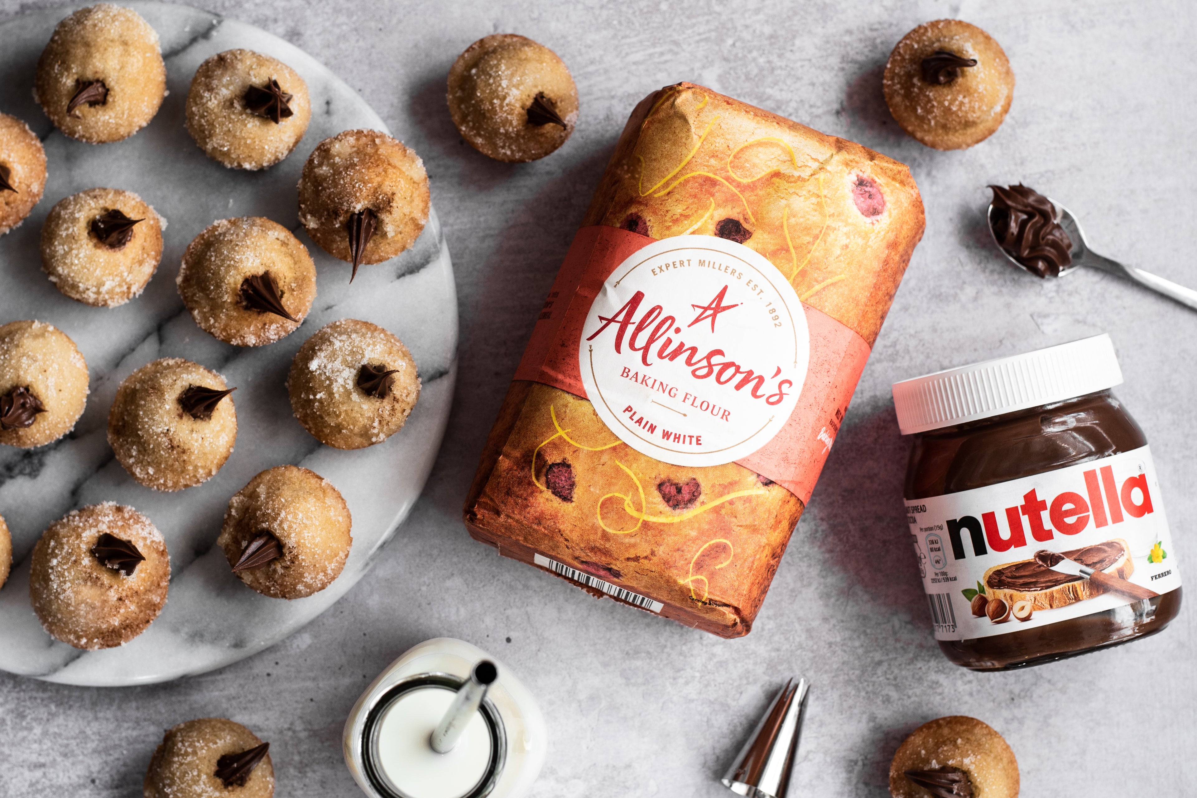 Plate of Nutella filled doughnuts next to a jar of Nutella and bag of flour