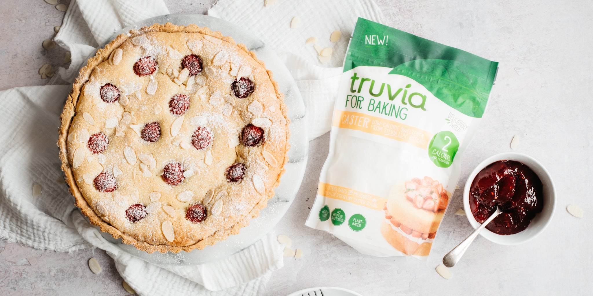 Bakewell tart on a cake plate with a pack of truvia for baking next to it and a pot of jam