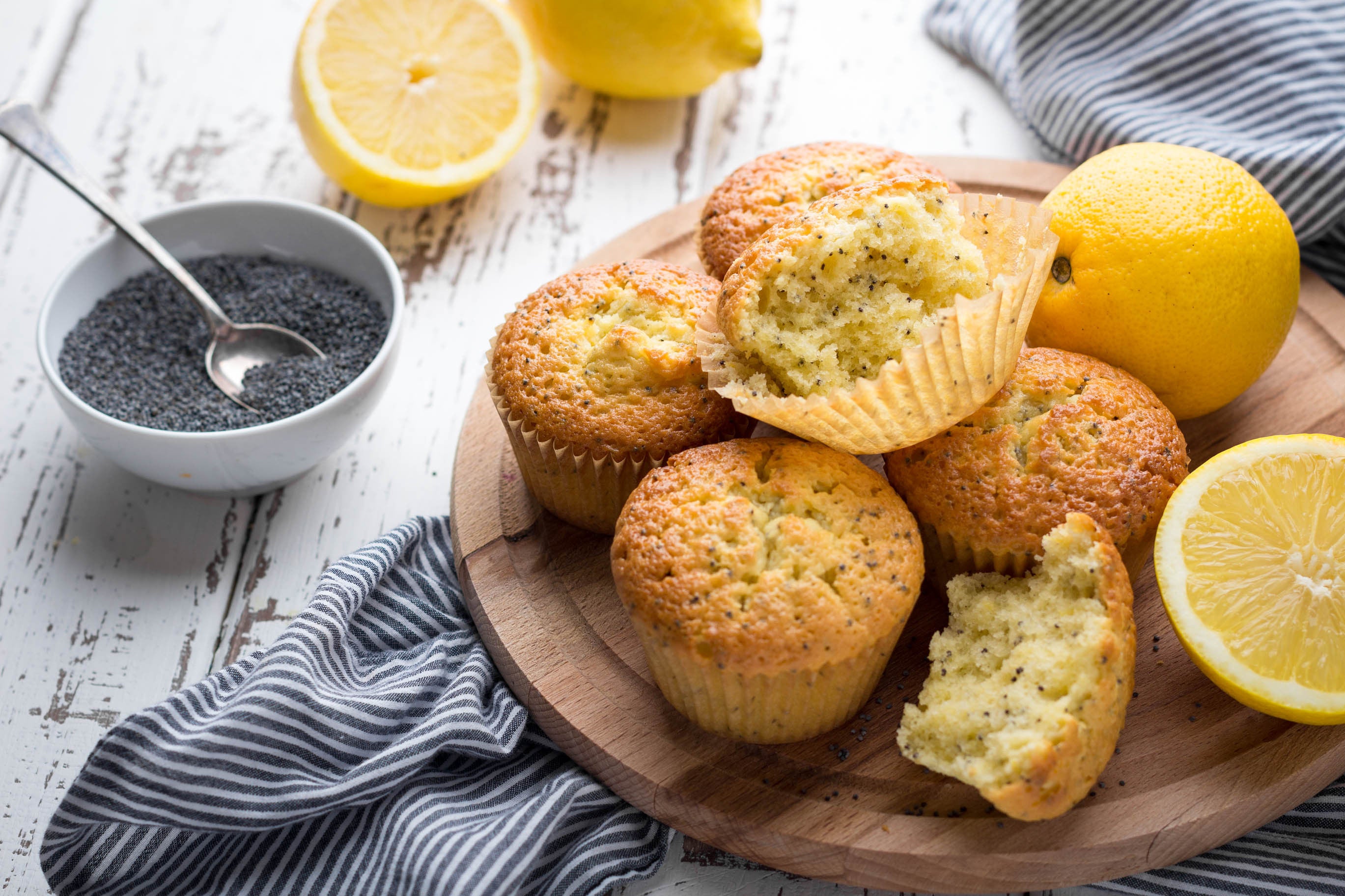 Lemon poppy seed muffins on a wooden chopping board next to a bowl of poppy seeds