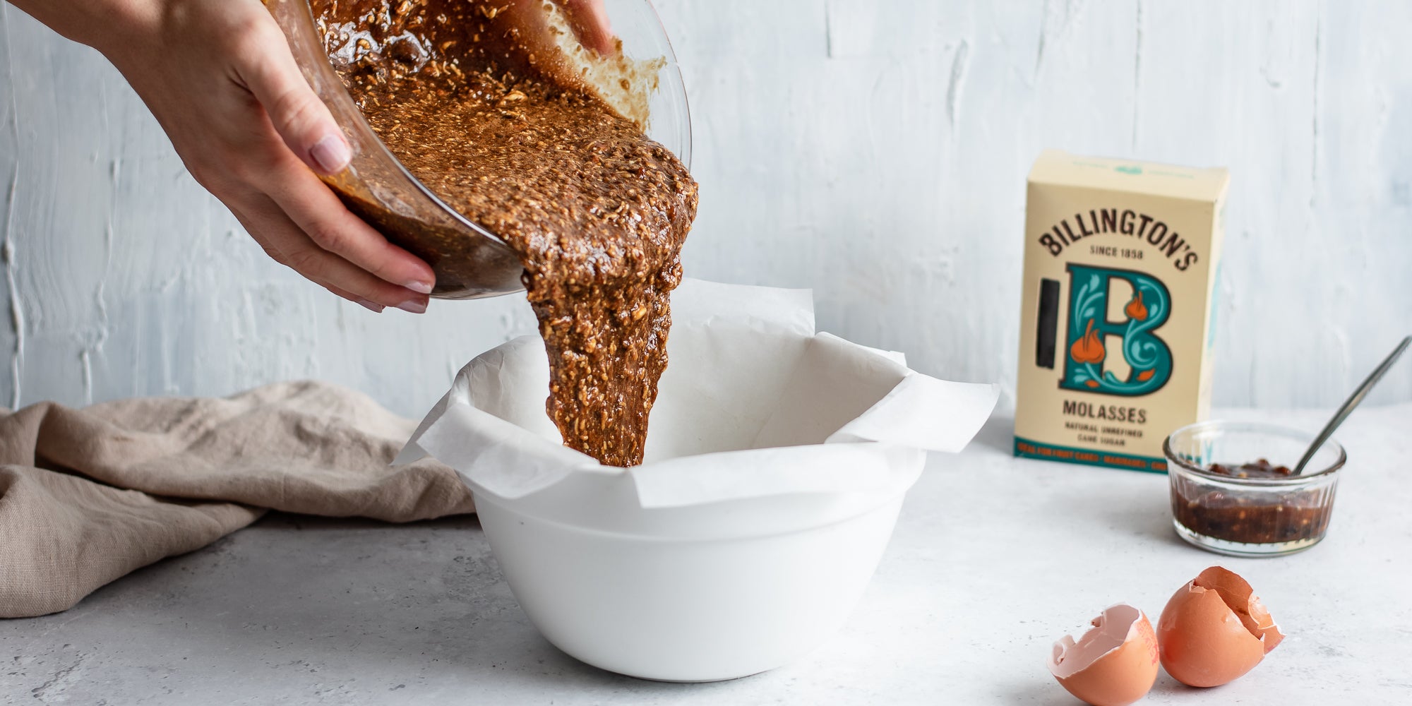 Action shot of making a Last Minute Christmas Pudding with the mixture being poured into a bowl, next to a box of Billington's Molasses