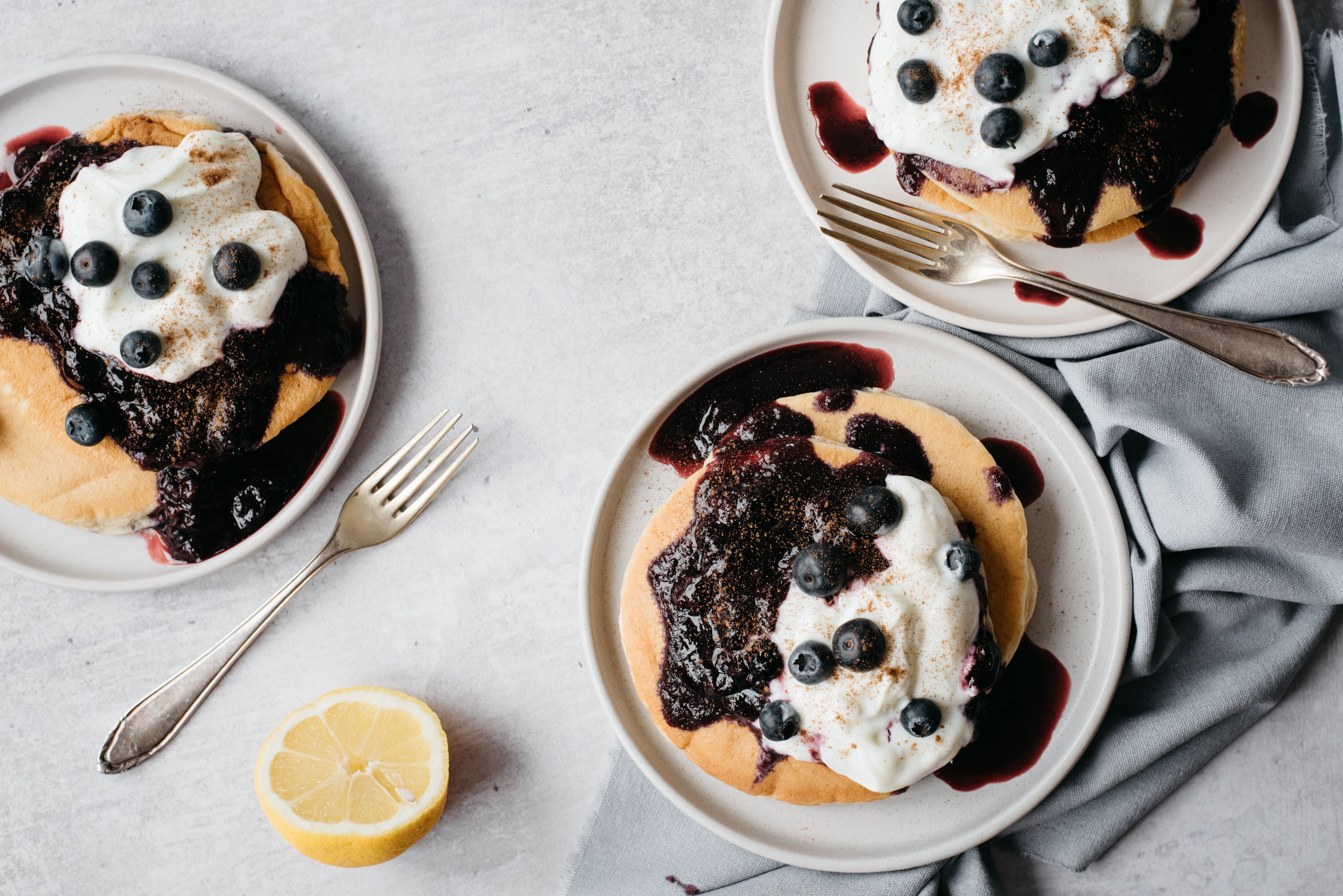 Top view of Cinnamon Pancakes with Blueberry Compote topped with yoghurt, blueberries and slice lemon