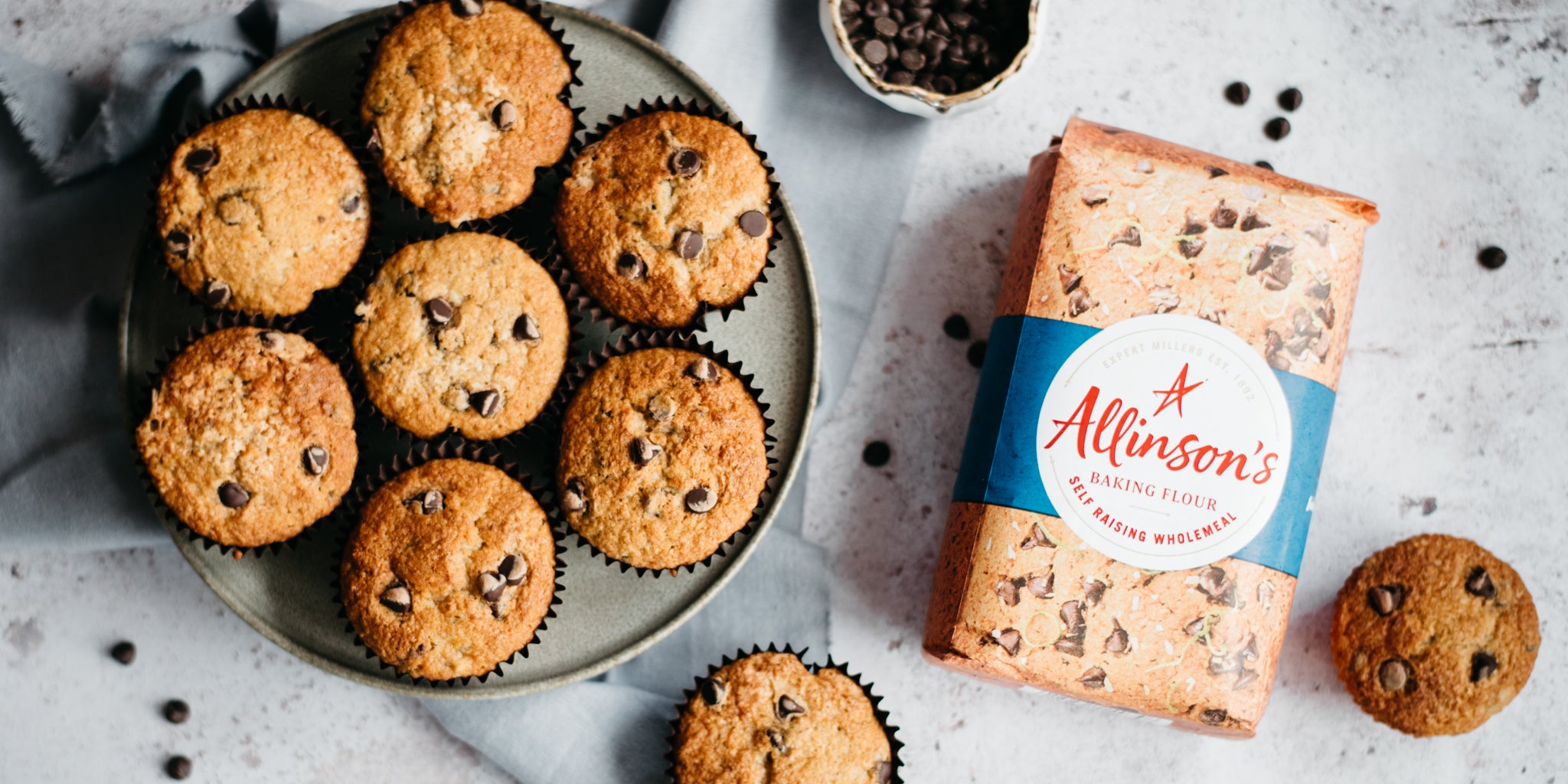 Top view of Wholemeal Banana & Chocolate Chip Muffins on a wire cooling rack next to a bag of Allinson's Wholemeal flour