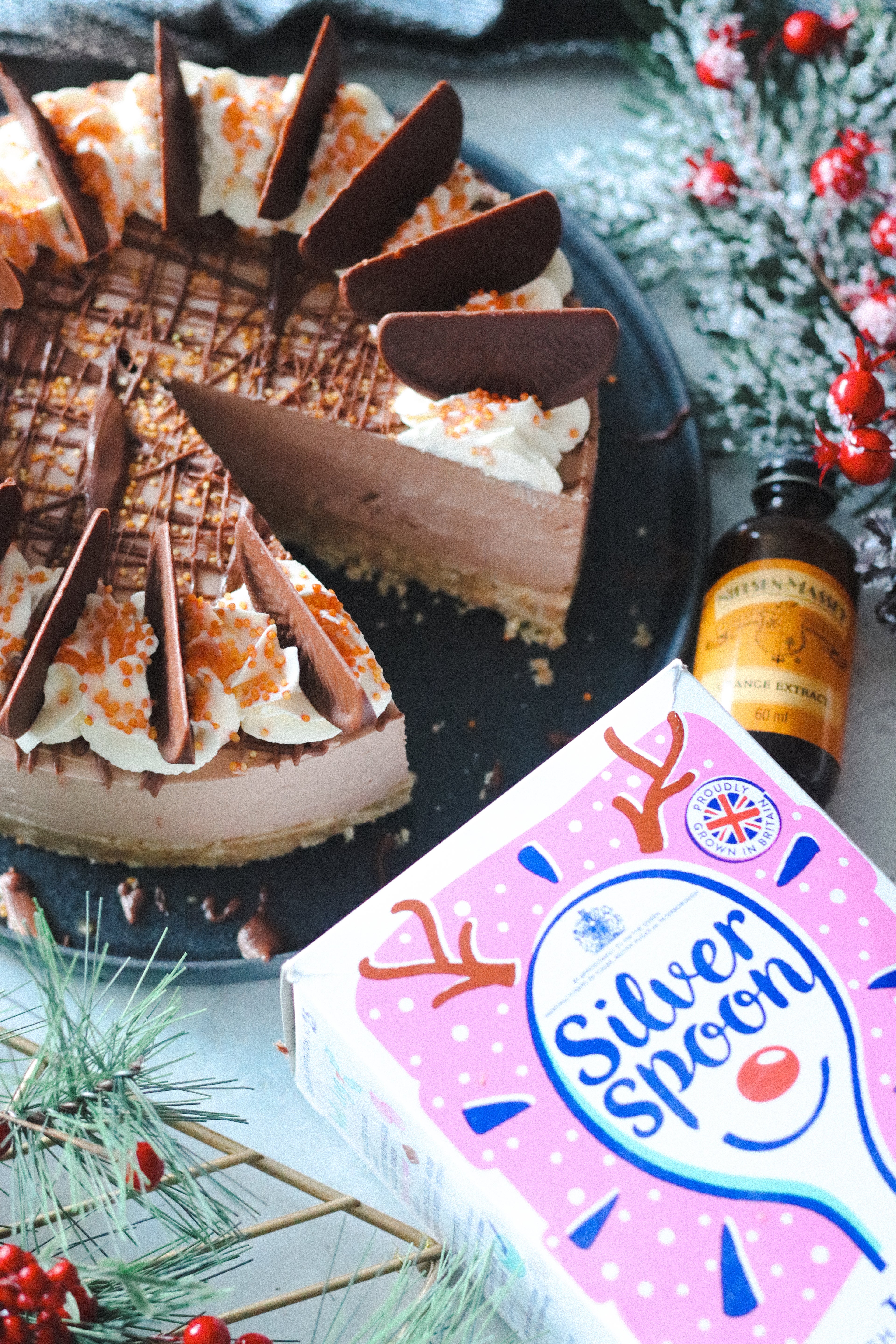 Top view of Chocolate Orange Cheesecake next to a box of Silver Spoon Icing Sugar, and a bottle of Nielsen-Massey Orange extract