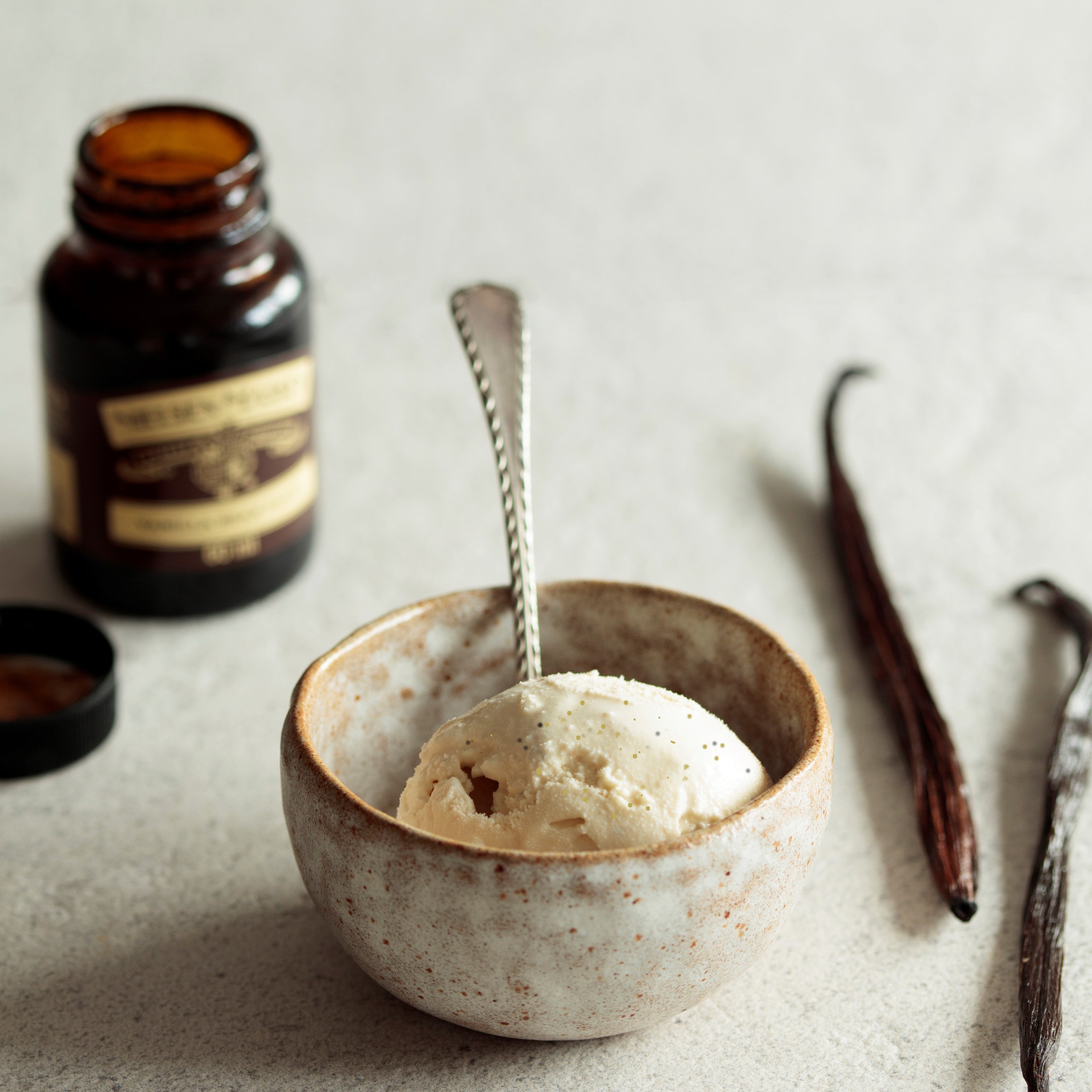 Bowl of vanilla ice cream next to a bottle of vanilla essence