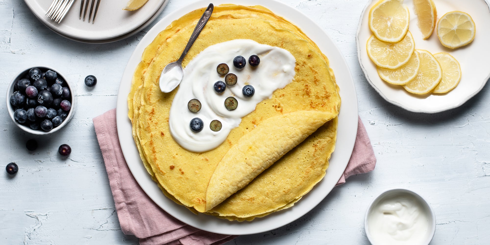 Top down view of yoghurt smothered onto a turmeric and lemon pancake and blueberries sprinkled on top