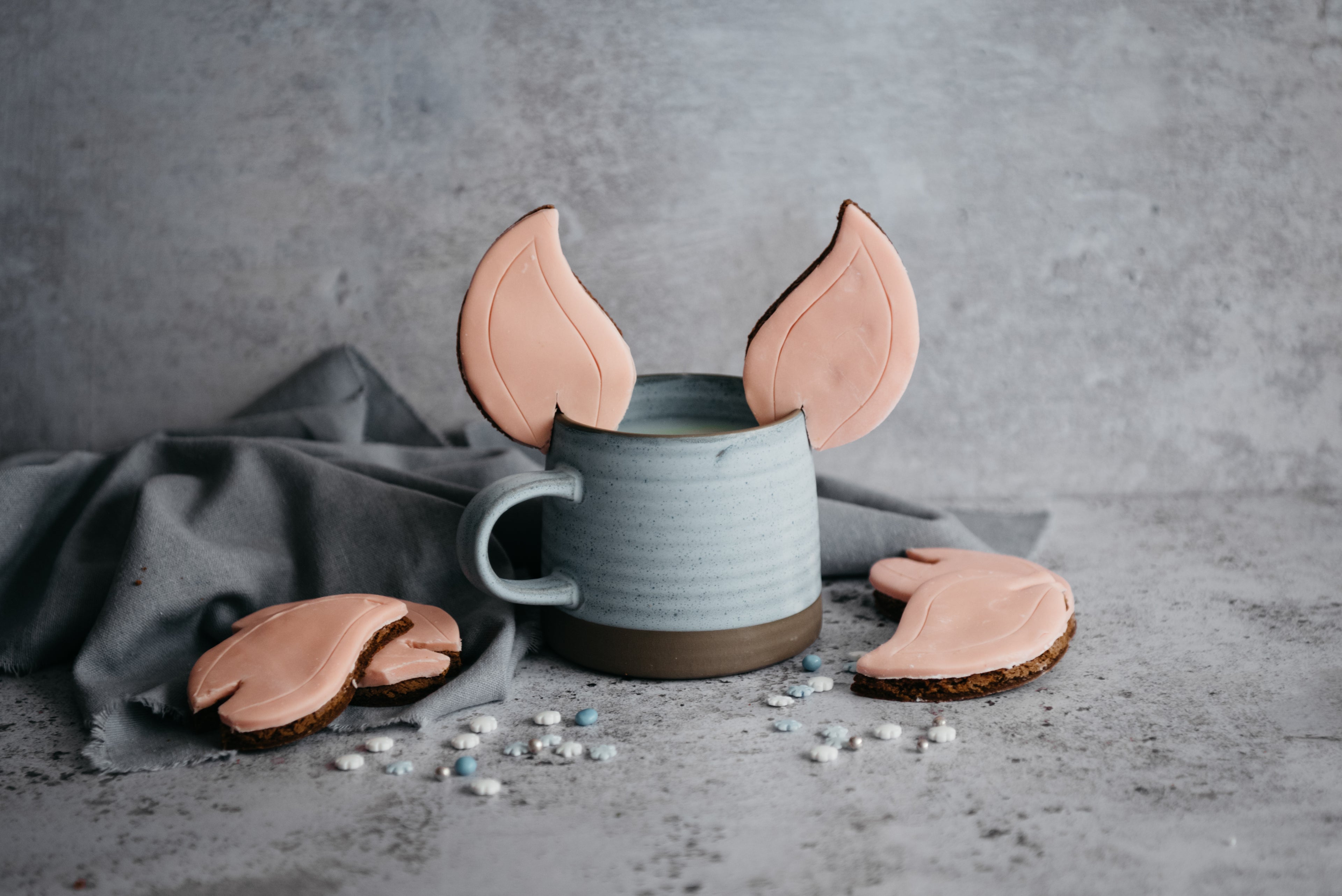 Elf Ears Gingerbread Cookies on the edge of a blue mug, next to more Elf Ears Gingerbread Cookies scattered around