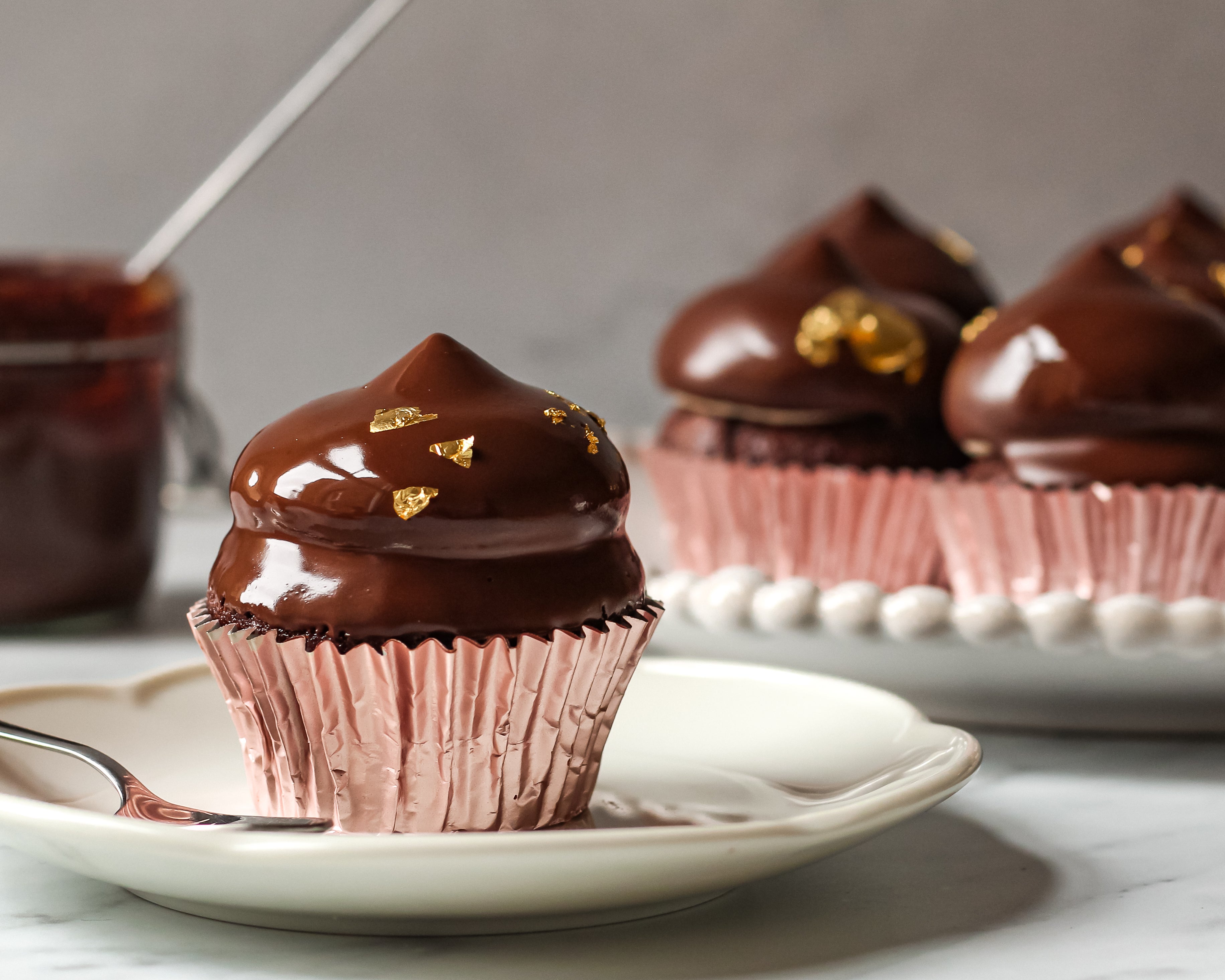 Close up of Hi-Hat Cupcakes coated in glossy vegan chocolate dip and gold flakes, next to a fork ready to eat