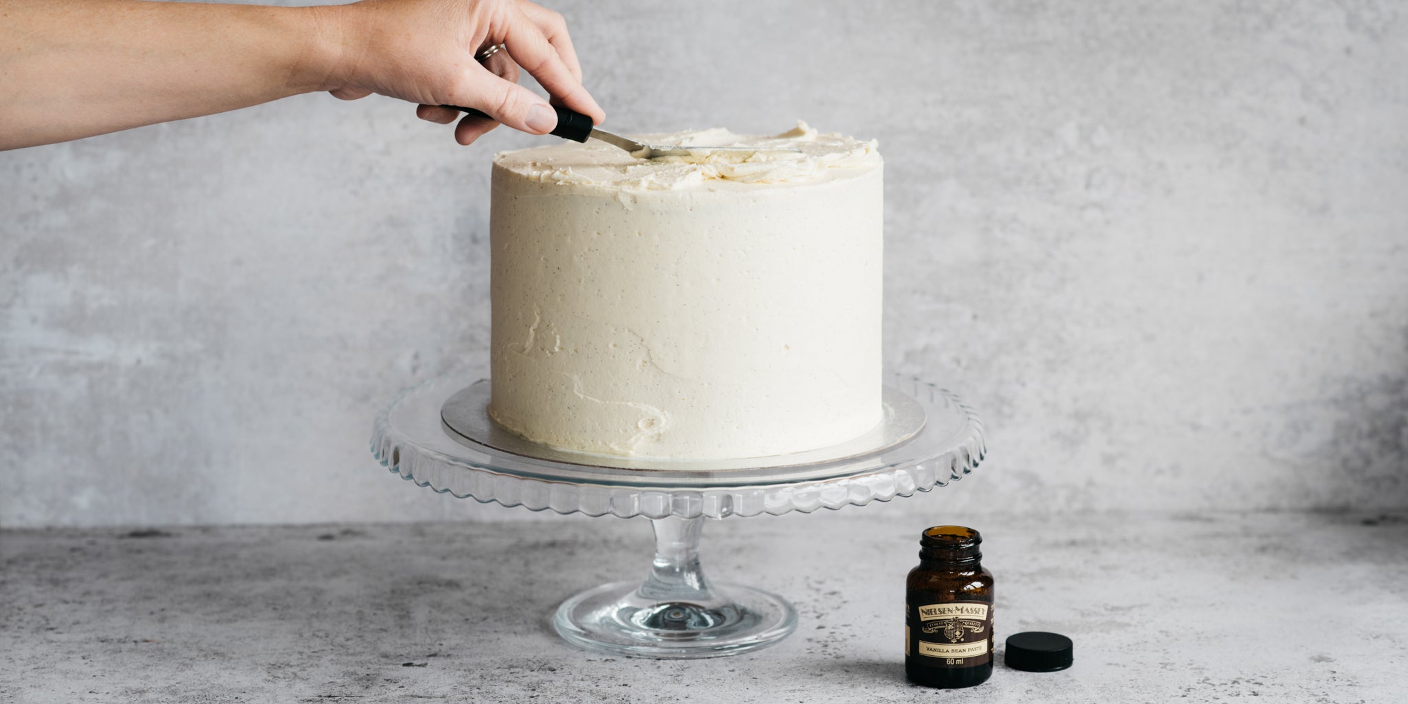 Side on view of an ultimate vanilla celebration cake and a bottle of Nielsen Massey vanilla bean paste