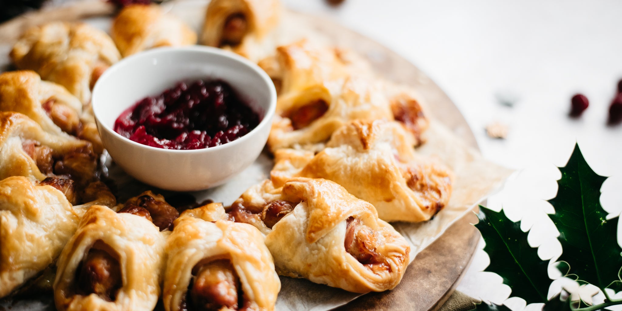 A side on view of a tray of cooked pigs in duvets with cranberry sauce dip