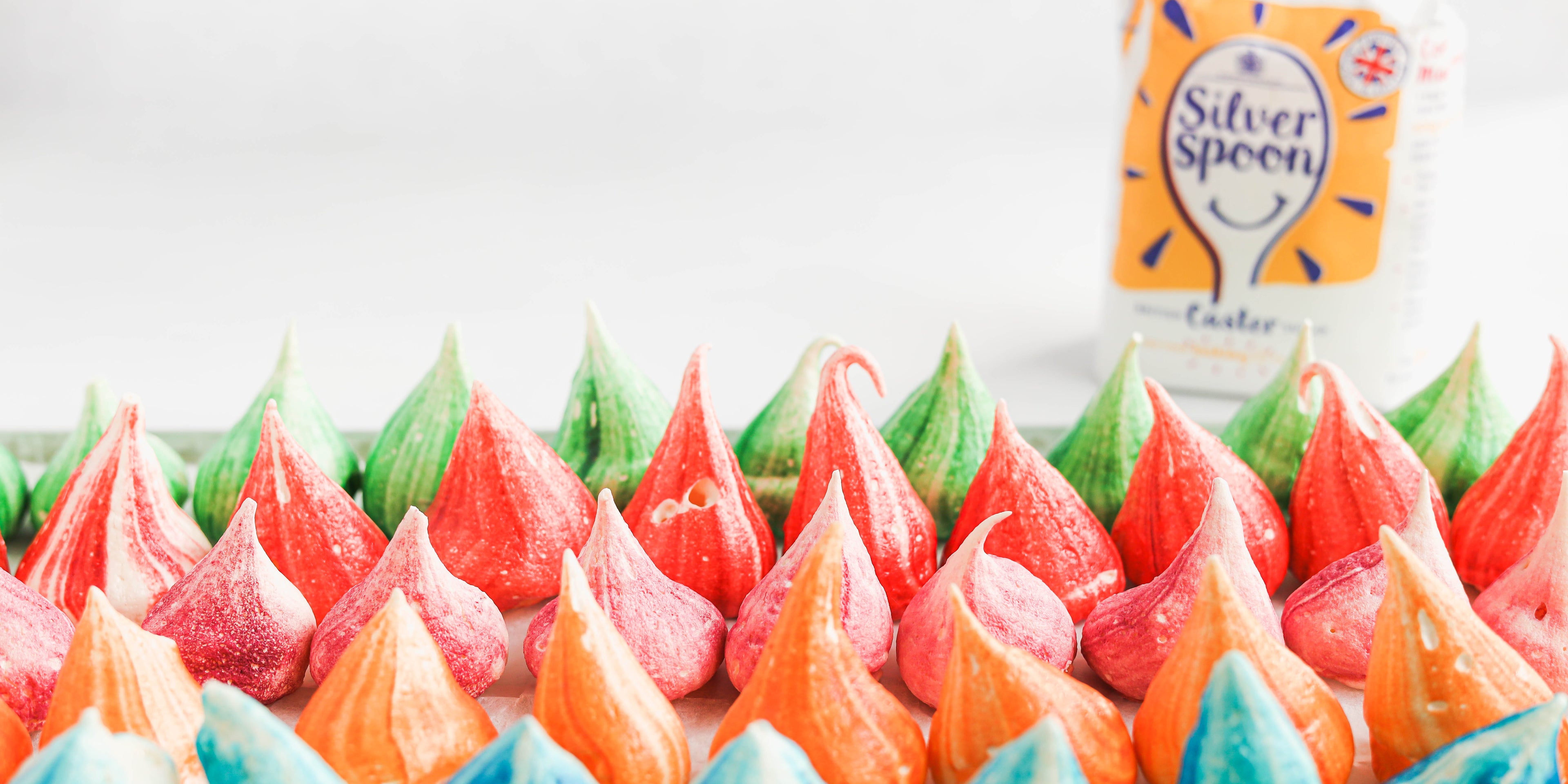 Top view of the peaks of Rainbow Meringues with a bag of silver spoon caster sugar in the background