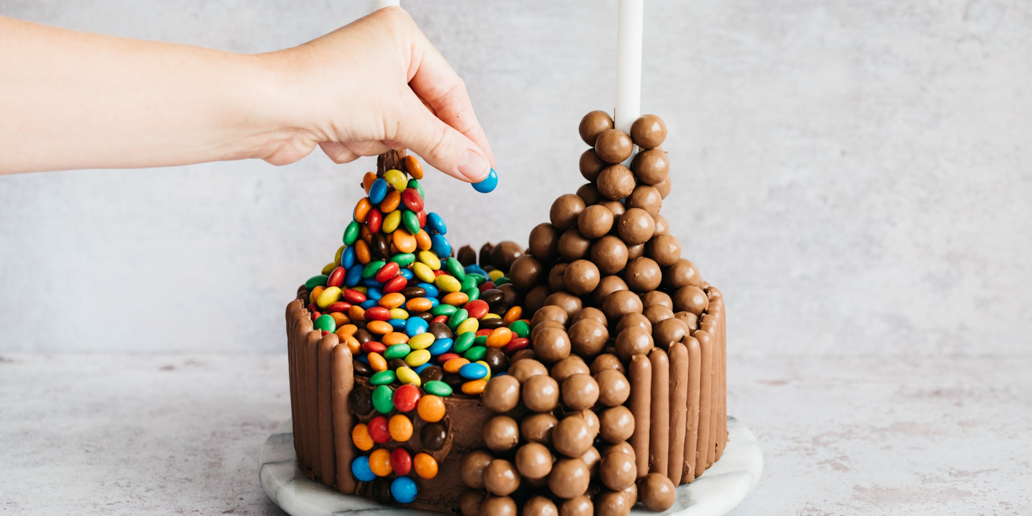 Chocolate Showstopper Cake being hand decorated with M&M's and Maltesers on dole rods