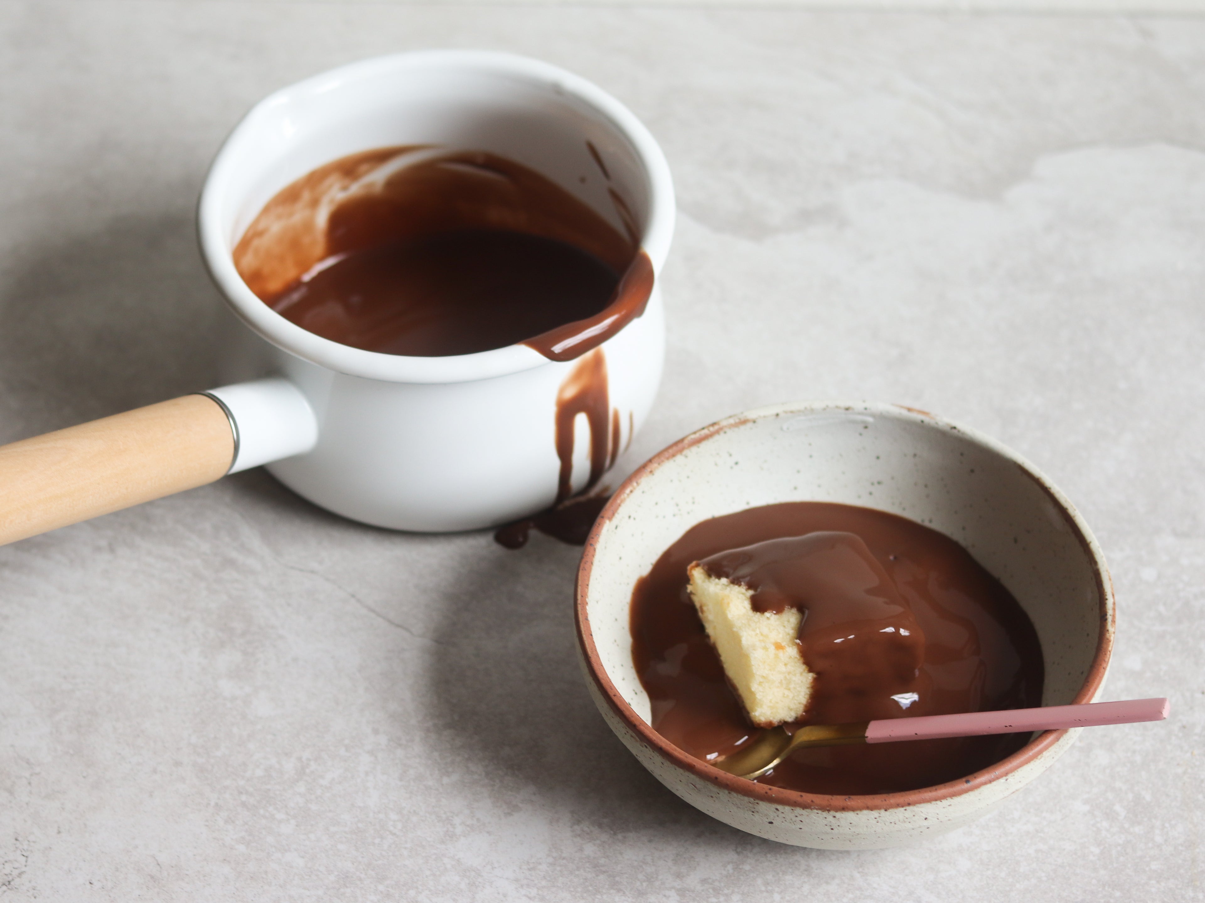 Chocolate Custard next to a bowl of sponge cake covered in chocolate custard, with a spoon ready to serve